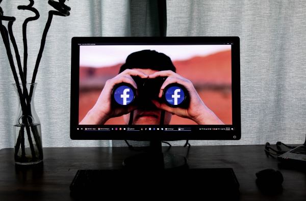 Facebook Pay: imagem de um monitor de computador com uma pessoa na tela usando um binóculo com o logo do Facebook nas lentes.