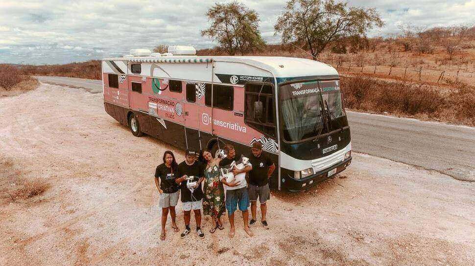 Transformação Criativa: imagem de um ônibus estacionado na estrada com as pessoas do projeto transcriativa do lado de fora, na frente do ônibus.