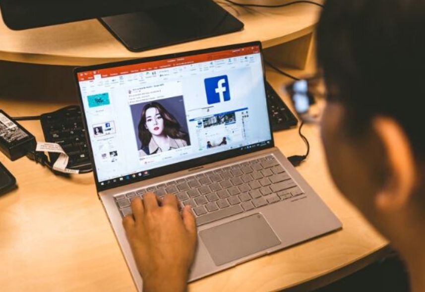 Novo Facebook 2020: imagem de uma pessoa sentada acessando o facebook pelo notebook que está apoiado em um mesa.