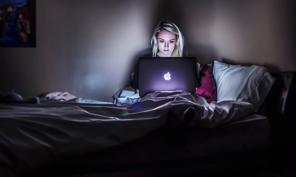 Desenvolvimento pessoal e profissional: imagem de uma mulher loira dentro de um quarto, sentada na cama com um notebook no colo olhando para tela