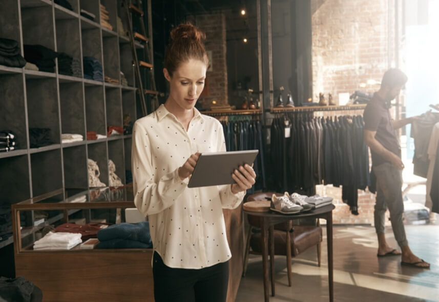 como atrair clientes para loja de roupas: imagem de uma mulher, dentro de uma loja de roupas, segurando um tablete nas mãos