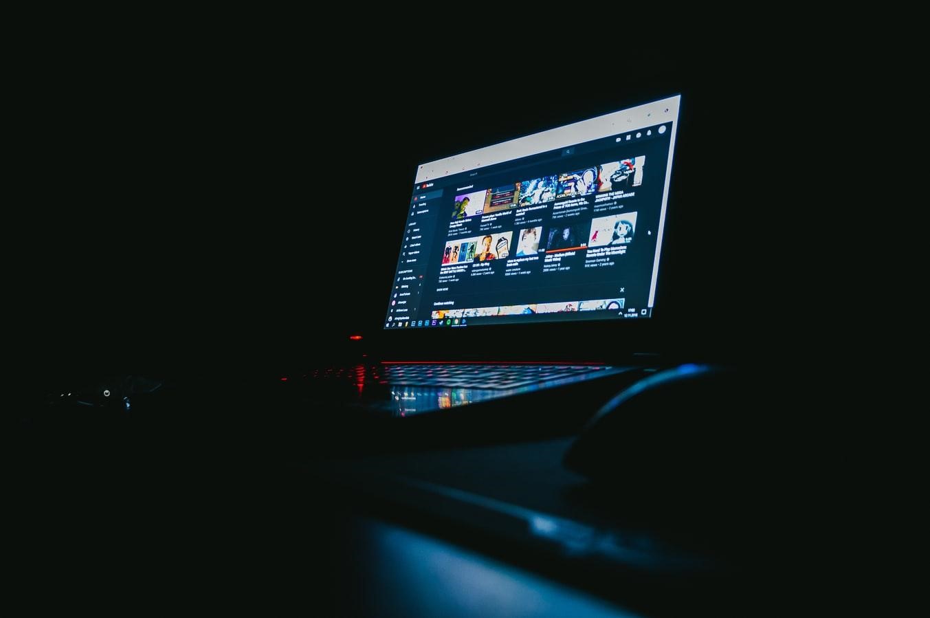 Canal no youtube: imagem de um notebook com a tela aberta em cima de uma mesa com a luz apagada dando destaque para o monitor