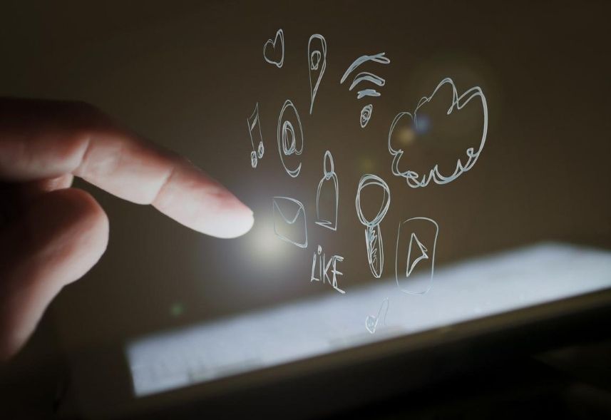 Social commerce: imagem de um dedo em direção a tela de um celular com ícones de wifi, nuvem, arroba e curtidas saindo da tela.
