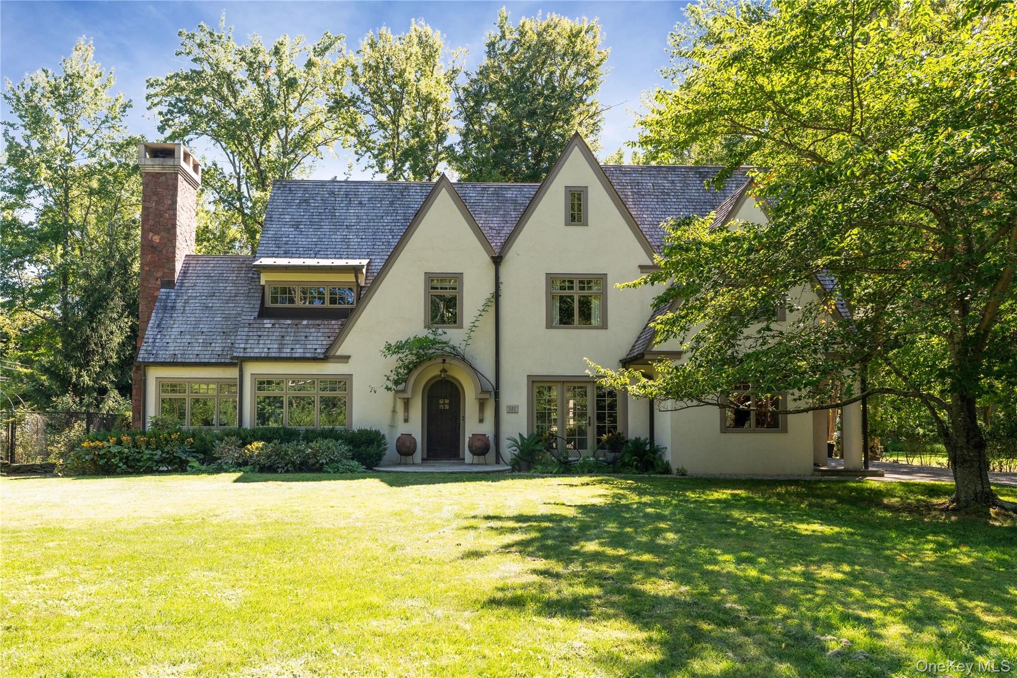 THE GABLES - There are homes that simply exist & there are homes that tell a story. The Gables, a historic Tudor originally built in 1929 by the Johnson family & thoughtfully expanded by noted architect Jo Machinist in 2004, is very much the latter - a place where the past is honored, every beam & stone seems to carry memory & where life unfurls in quiet elegance. Situated in the rarefied hamlet of Sneden&rsquo;s Landing, The Gables offers something singular: a serene retreat just beyond the city&rsquo;s edge, where privacy, artistry & natural beauty converge. Sneden&rsquo;s Landing has long been a sanctuary for those seeking both discretion & inspiration. Nestled along the Hudson River & embraced by forested cliffs, it has drawn painters, writers & performers for generations - its proximity to Manhattan a mere 20+ minutes, yet its spirit a world apart. Here, history lingers... From the nearby Palisades Free Library to the clay courts of the residents-only Sneden&rsquo;s Landing Tennis Association, the hamlet offers a community steeped in tradition. The neighboring river towns of Piermont & Nyack, with their galleries, riverfront cafes & fine dining, extend the charm just minutes away. Stepping inside The Gables feels less like entering a house & more like arriving in a well-worn novel, one written in warm light & timeless texture. Interiors & grounds have been shaped by the nationally recognized design team Tersigni Palachek, whose work lends a lived-in sophistication - an atmosphere akin to slipping into a favorite cashmere sweater. Nearly 3, 000 SF of living space is suffused with natural light, where vaulted ceilings lift the spirit & the hand-laid Rockland brownstone fireplace anchors the heart of the home. Hardwood floors of reclaimed hand hewn heart pine run throughout, carrying a warmth that is both grounding & enduring. The first floor unfolds with grace: a grand yet intimate living room with radiant heat, glowing with sun & anchored by stone; a dining room dressed in Elitis leaf wall coverings & Venetian silk Fortuny pendants; a kitchen where form & function meet at the highest level, complete with marble countertops & an expansive island where conversations over morning coffee happen with ease. High end appliances complete the space. Even the powder room holds artistry, with walls custom painted by Palachek. Three bedrooms crown the second floor, including a primary suite that offers sanctuary: its spa-like bath, with double vanity, soaking tub, radiant heat & impeccable fixtures, promises restorative stillness. Outdoors, the European-inspired gardens unfold like poetry: daffodils, lilacs, peonies, rhododendron, Japanese maple - speak to generations past, drawn from the very soil of Sneden&rsquo;s Landing & its neighboring gardens. Japanese cherry trees bloom in spring with extraordinary grace, while the organic vegetable garden invites a sustainable rhythm of life. Whether an intimate dinner on the terrace or a gathering of a 100 guests beneath the open sky, the grounds invite celebration as naturally as they do solitude. The detached two-car garage, with its finished studio above, offers an ideal escape for guests, artists or the modern remote worker. A 220 EV charger, whole-house generator & updated mechanicals reflect the care & investment that have kept the home impeccably maintained, as turn-key as it is timeless. The lower level provides practicality with a spacious laundry room, while the unfinished attic, currently a home gym, holds promise for future expansion. At The Gables, life balances between refinement & ease, history & modernity, city proximity & country peace. It is a residence for those who seek discretion, artistry & seclusion. Just 12 miles from the GW Bridge, yet enveloped in the privacy of Sneden&rsquo;s Landing, 141 Washington Spring Rd stands ready for its next stewards. Those who will continue its legacy will find themselves woven into the quiet, luminous fabric of this extraordinary home.