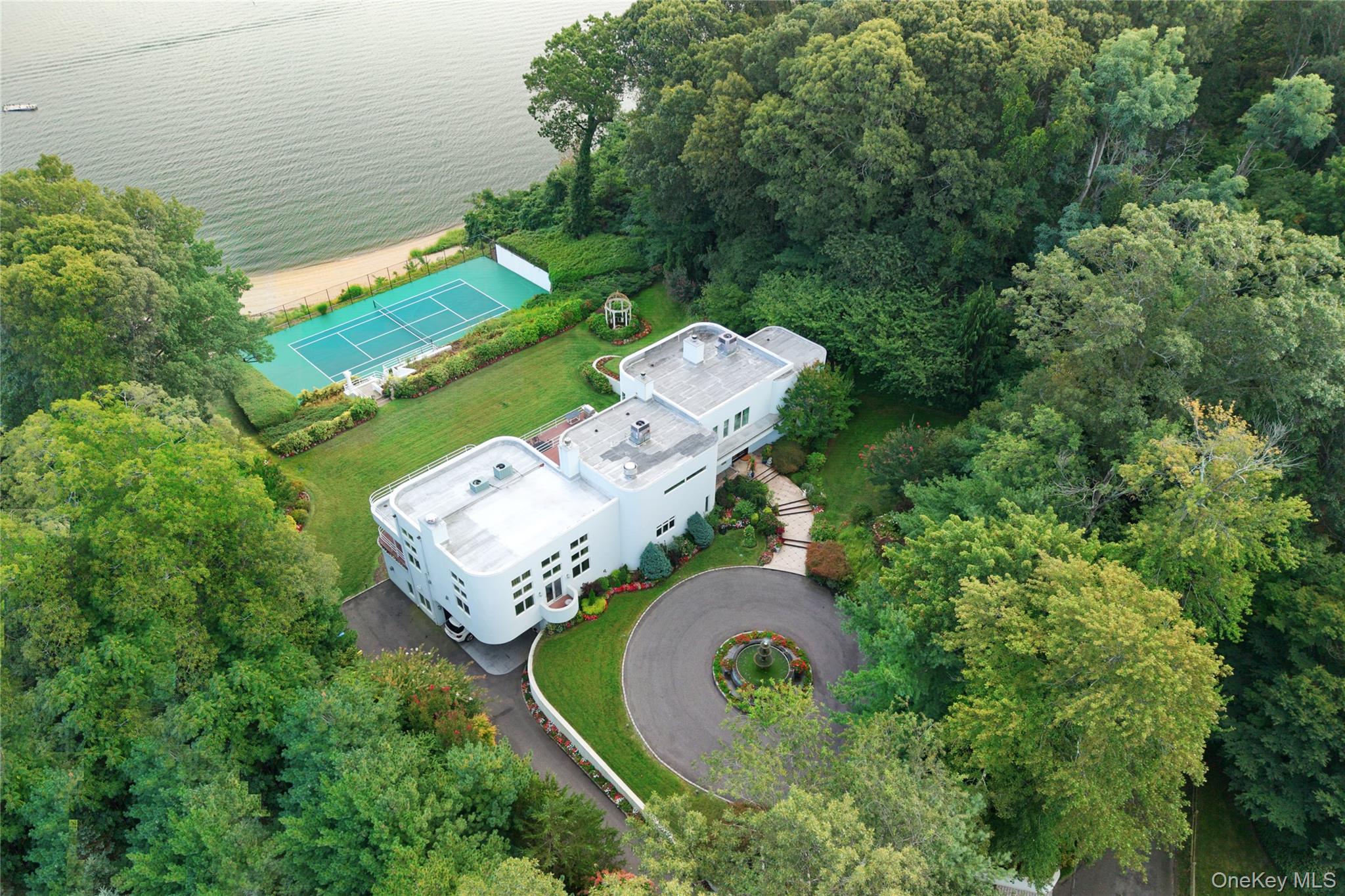 Experience the ultimate in waterfront living with this extraordinary 9, 000+ sq. ft. estate set on two sweeping acres with 200 feet of private shoreline in Oyster Bay. Designed for both grand entertaining and everyday comfort, the residence offers 5 bedrooms, 6.5 baths, and 4 fireplaces, all supported by modern essentials including a full-house generator and security system.Step inside the dramatic entry foyer where light and space unfold into expansive living areas with floor-to-ceiling windows framing panoramic water views. The main level is highlighted by a sophisticated living room, formal dining room, and a versatile lounge/meeting space. A library with its own bath provides a perfect retreat or guest option. The chefâ€™s kitchen impresses with granite counters, custom cabinetry, professional appliances including three ovens and two dishwashers, and an adjoining laundry/mudroom. A spectacular 1, 600 sq. ft. great room with a wet bar and wood-burning fireplace anchors the first floor.Upstairs, three ensuite bedrooms each open to private balconies overlooking the water. The primary suite is a true sanctuary featuring a fireplace, spa bath with dual vanities, and an oversized walk-in dressing closet. Outdoor living is elevated with more than 1, 800 sq. ft. of wraparound decking, a tennis court, gazebo, and direct water access for kayaking, jet skiing, and more.The lower level extends the lifestyle with an indoor pool and hot tub, an entertainment space with wet bar, a full guest suite with private entrance, abundant storage, and a 4+ car garage. With meticulous craftsmanship and unparalleled amenities inside and out, this residence is not just a homeâ€”itâ€™s a private waterfront resort.