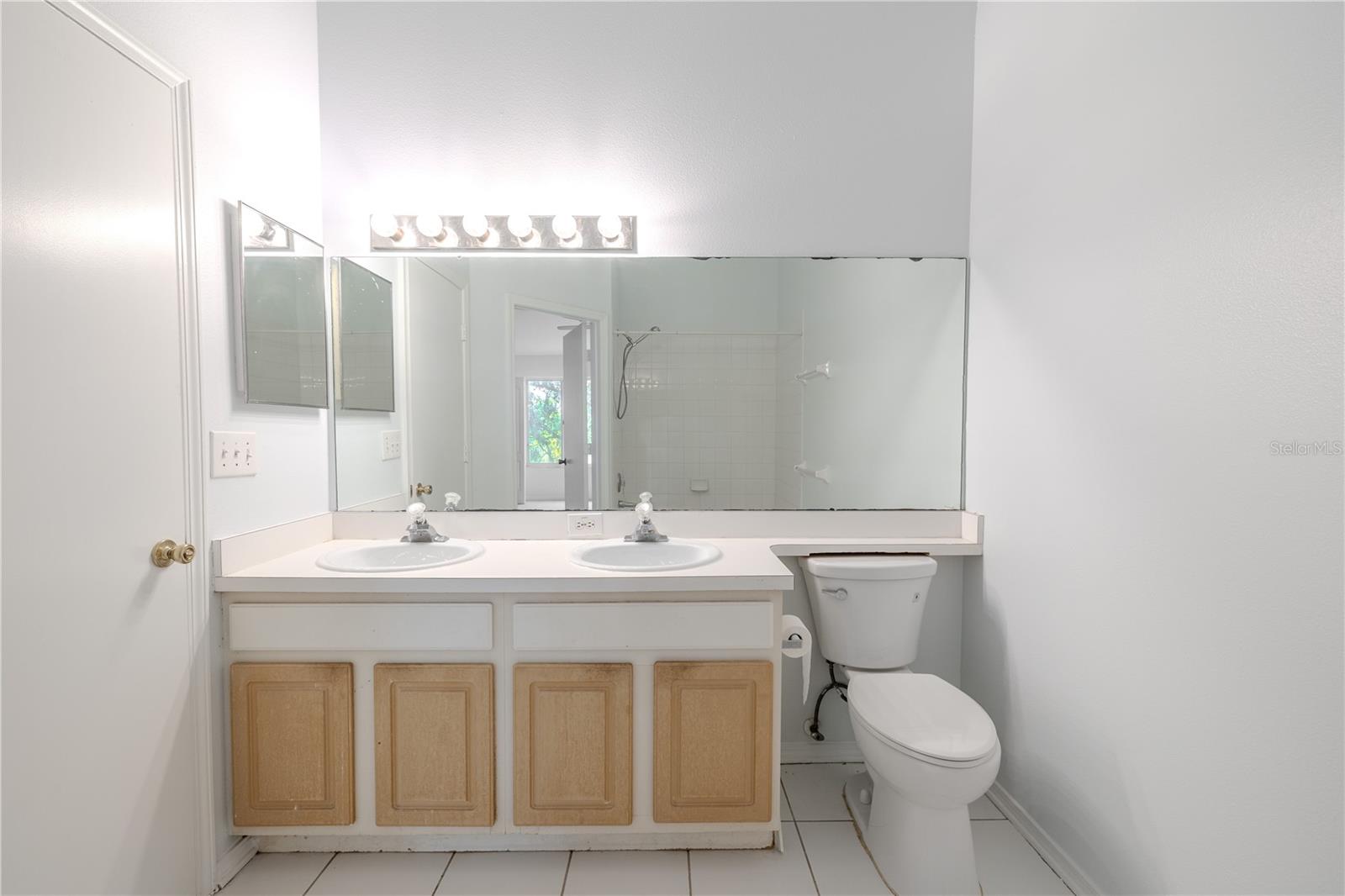 Shared 2nd floor bathroom features a mirrored vanity with dual sinks and storage, ceramic tile floor and a tub with shower.