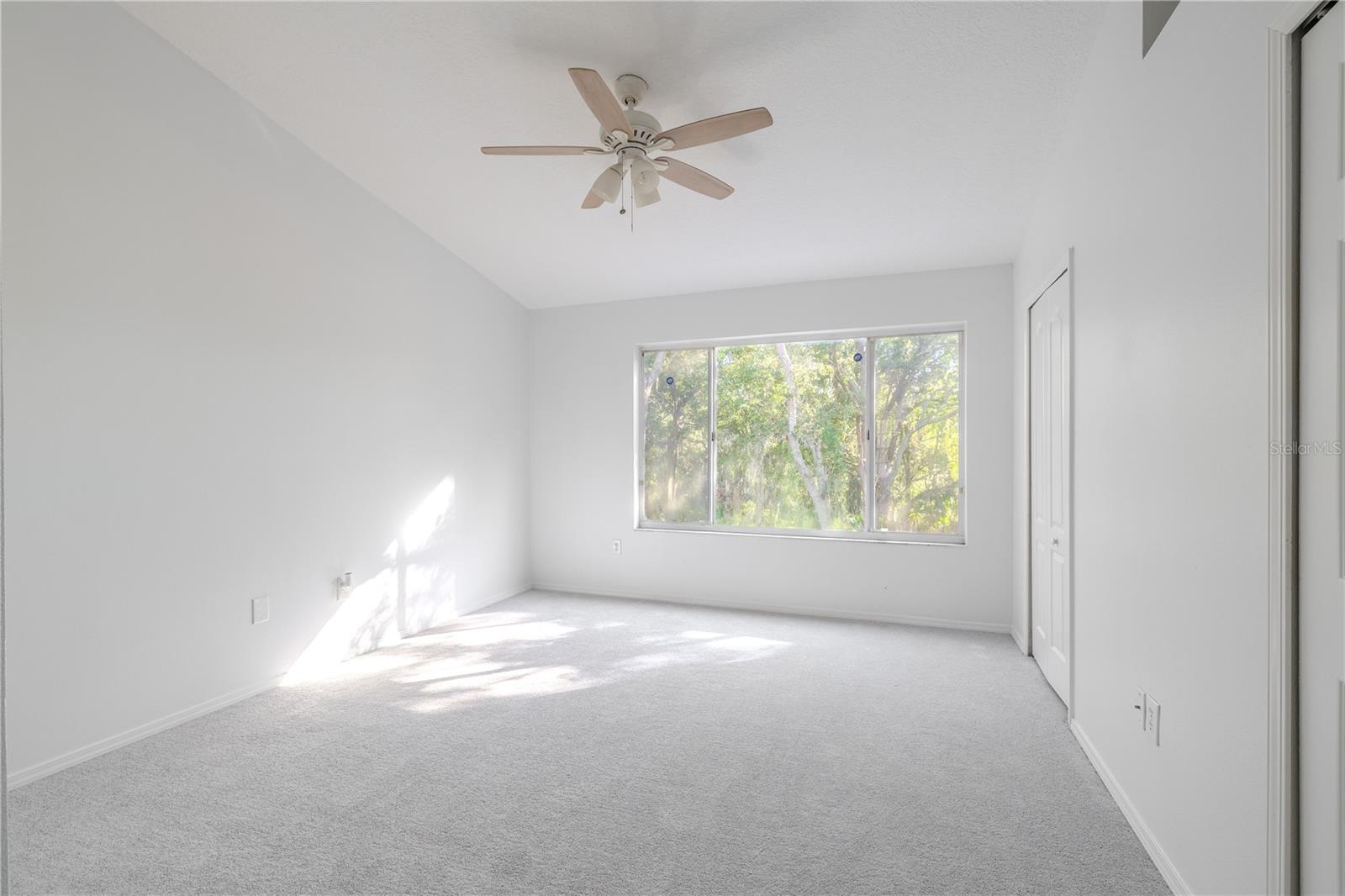 The Primary bedroom  features neutral tone walls and carpet, a ceiling fan with light kit and vaulted ceiling.