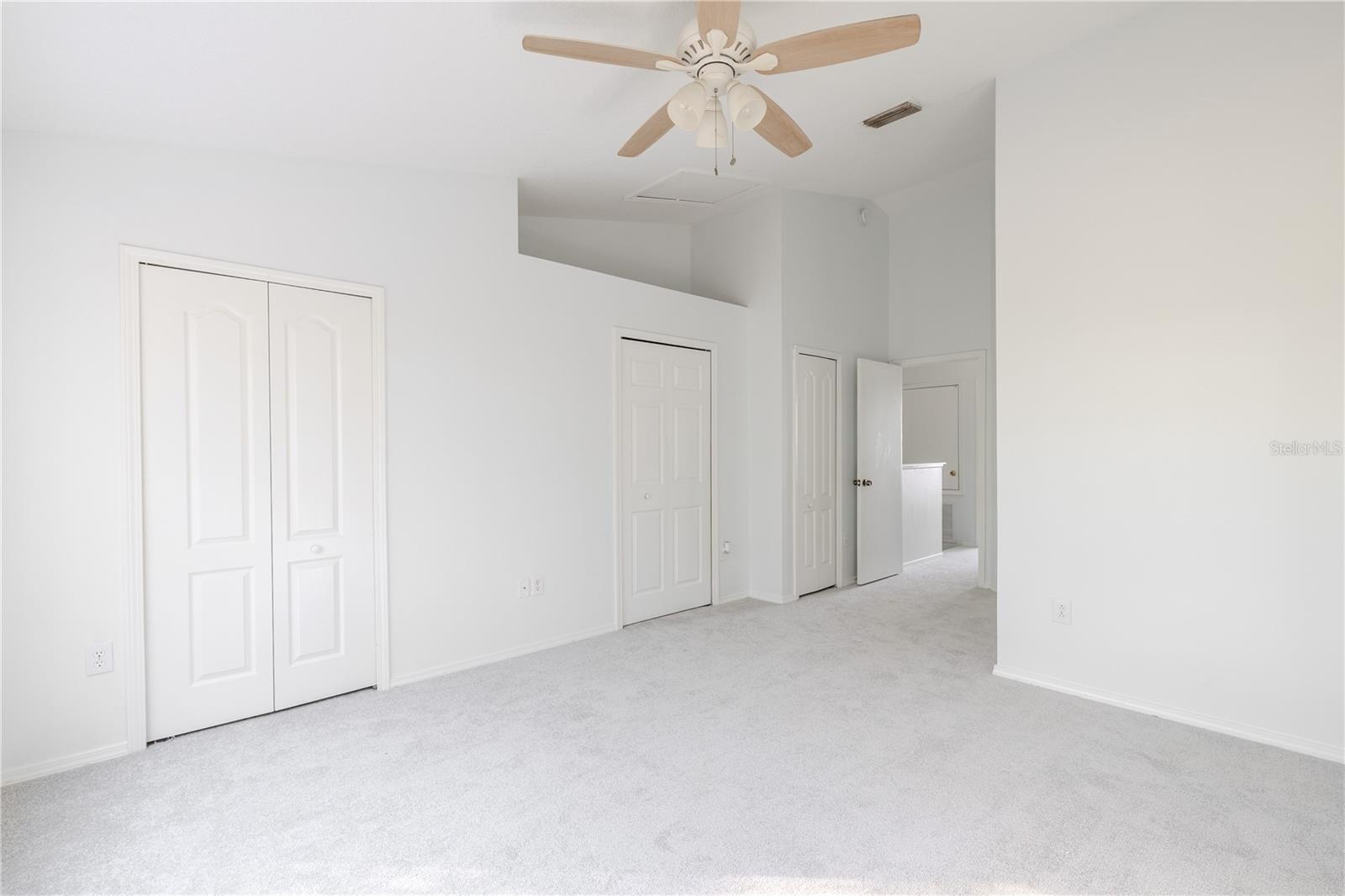 The Primary bedroom  features neutral tone walls and carpet, a ceiling fan with light kit and vaulted ceiling.