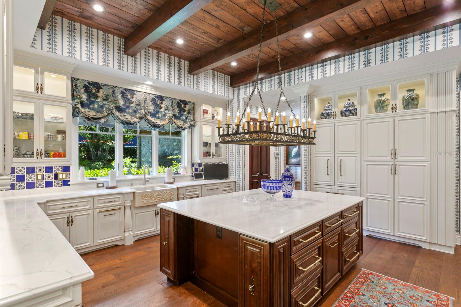 The kitchen is a masterpiece of design, featuring a statement chandelier that casts a warm glow over the expansive marble-topped island