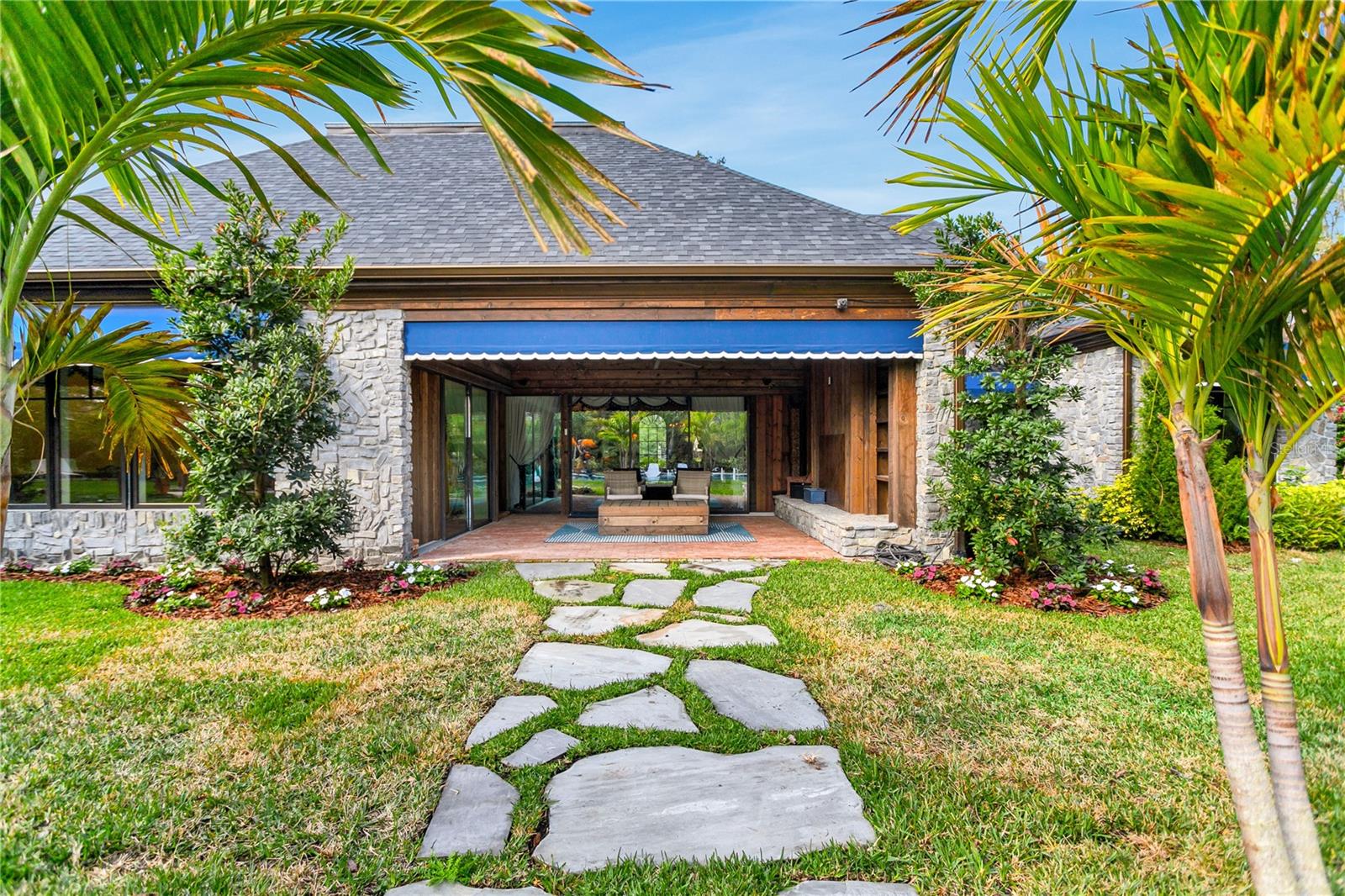As you approach the expansive patio, the stone path guides you through manicured gardens, flanked by tropical palms.