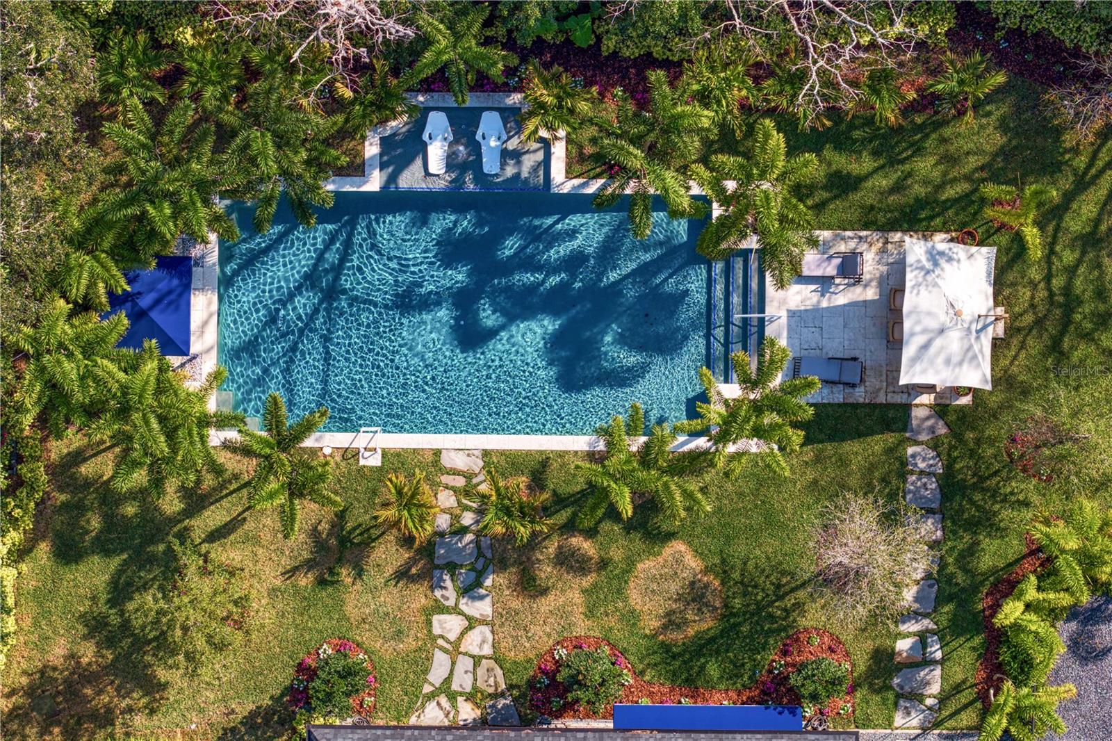 Step into a world of serenity where your backyard oasis greets you with a stunning, sprawling pool surrounded by lush greenery and elegant stone pathways.