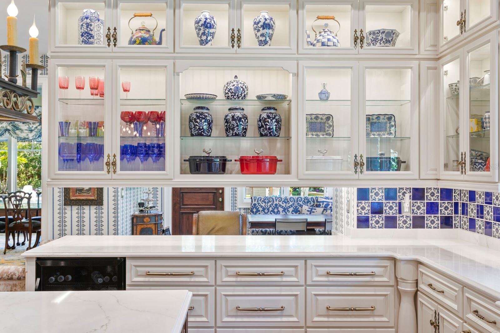 These custom cabinetry units, with their glass fronts, proudly display an exquisite collection of fine china and glassware, casting an artisanal glow across the room.