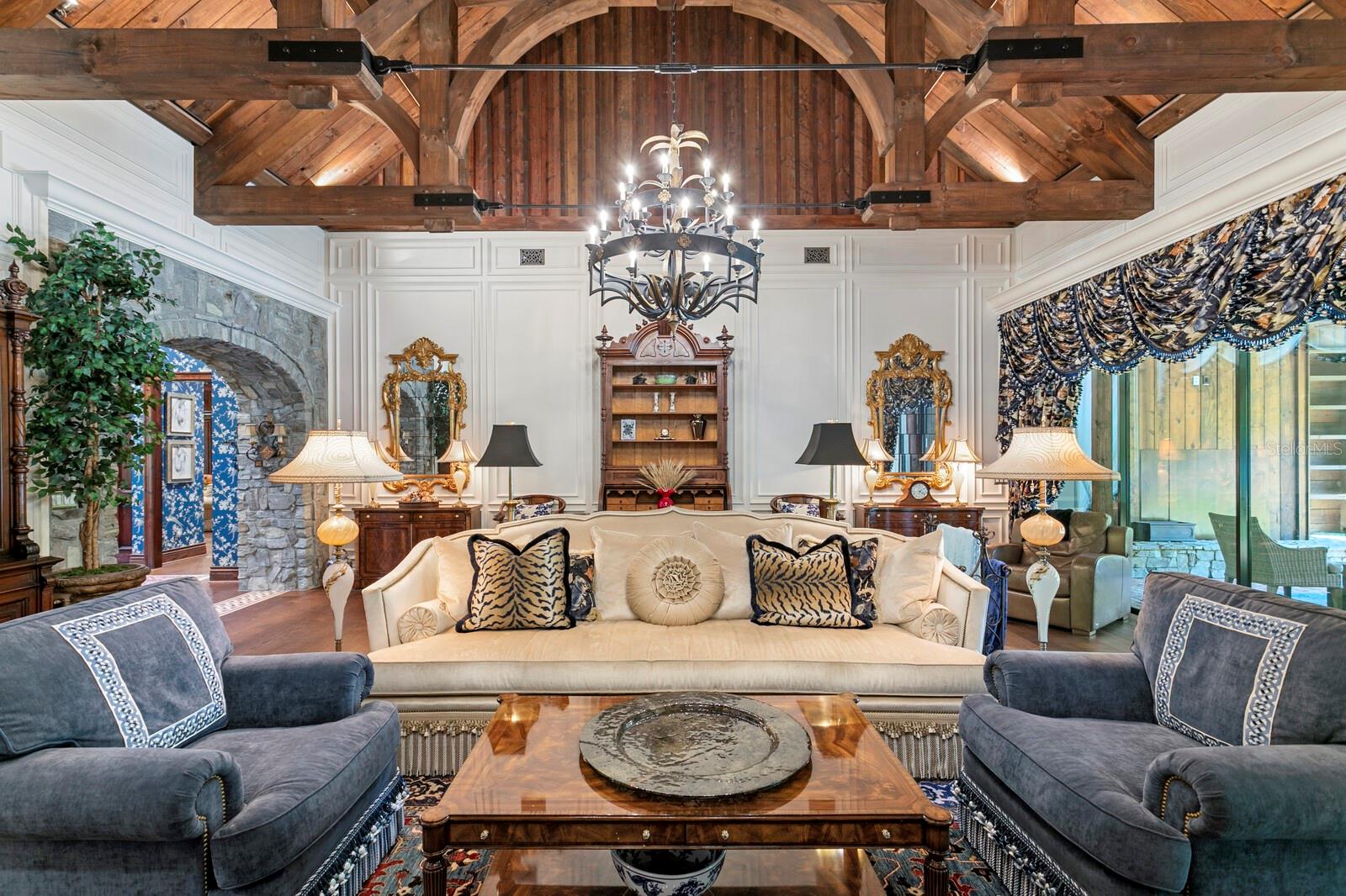 The living area showcases stunning exposed wood beams and a grand chandelier that dances with opulent charm above