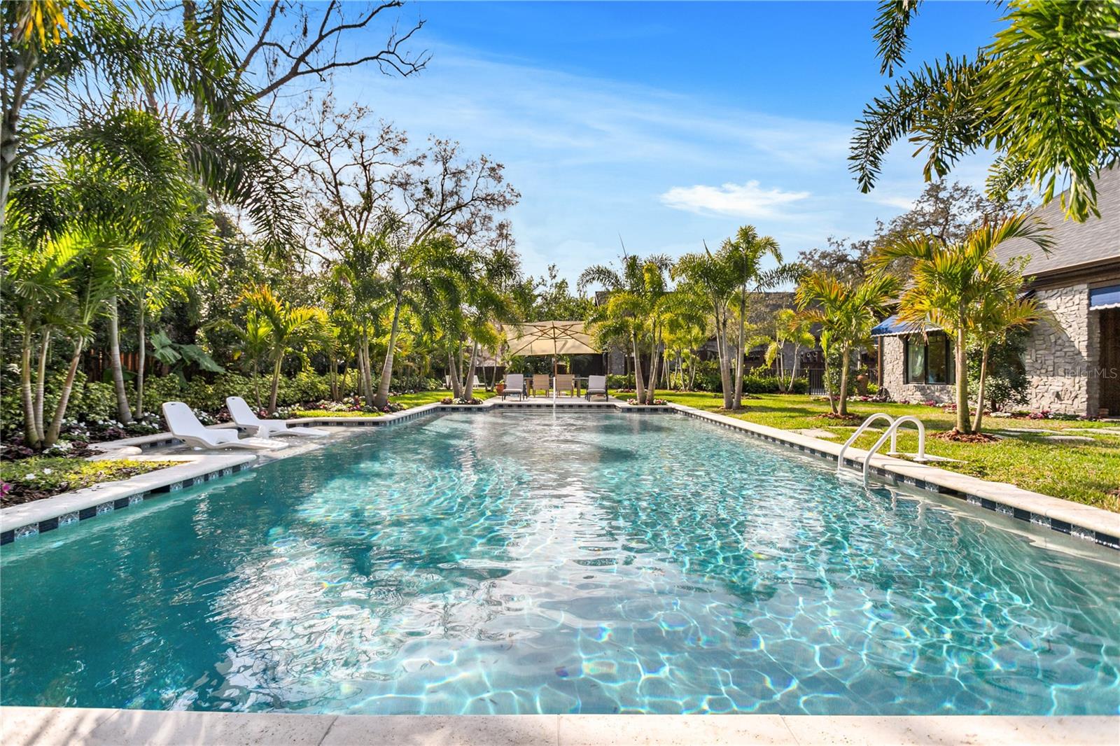 Nestled amidst lush greenery, this stunning backyard boasts an expansive pool that seems to merge seamlessly with the horizon, inviting you to dive into its crystalline waters.