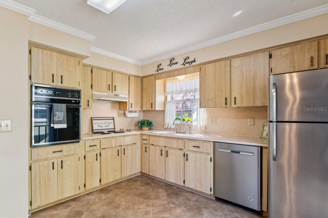 The kitchen features ceramic tile, crown molding, a wall oven, cooktop, dishwasher, and refrigerator.