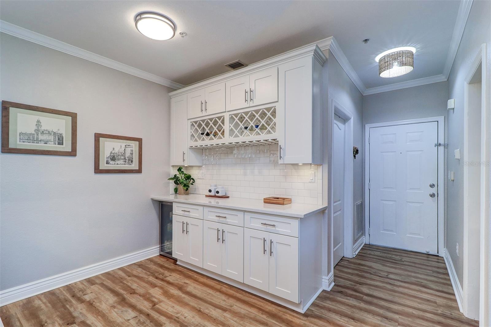 View of the front entry hall and the wine/coffee or dry bar with a wall of 42" upper and lower cabinets, wine rack, quartz counter tops, wine/beverage refrigerator to the far left