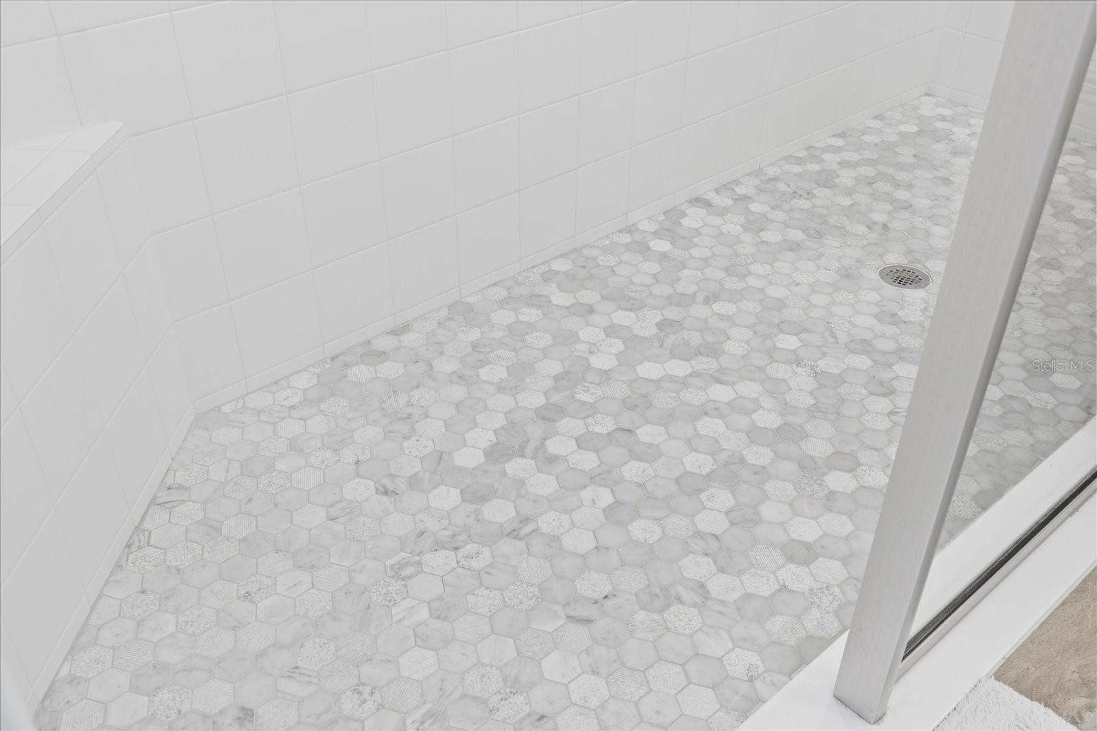 Corner shower seat and tiled shower floor with glass wall in primary bathroom