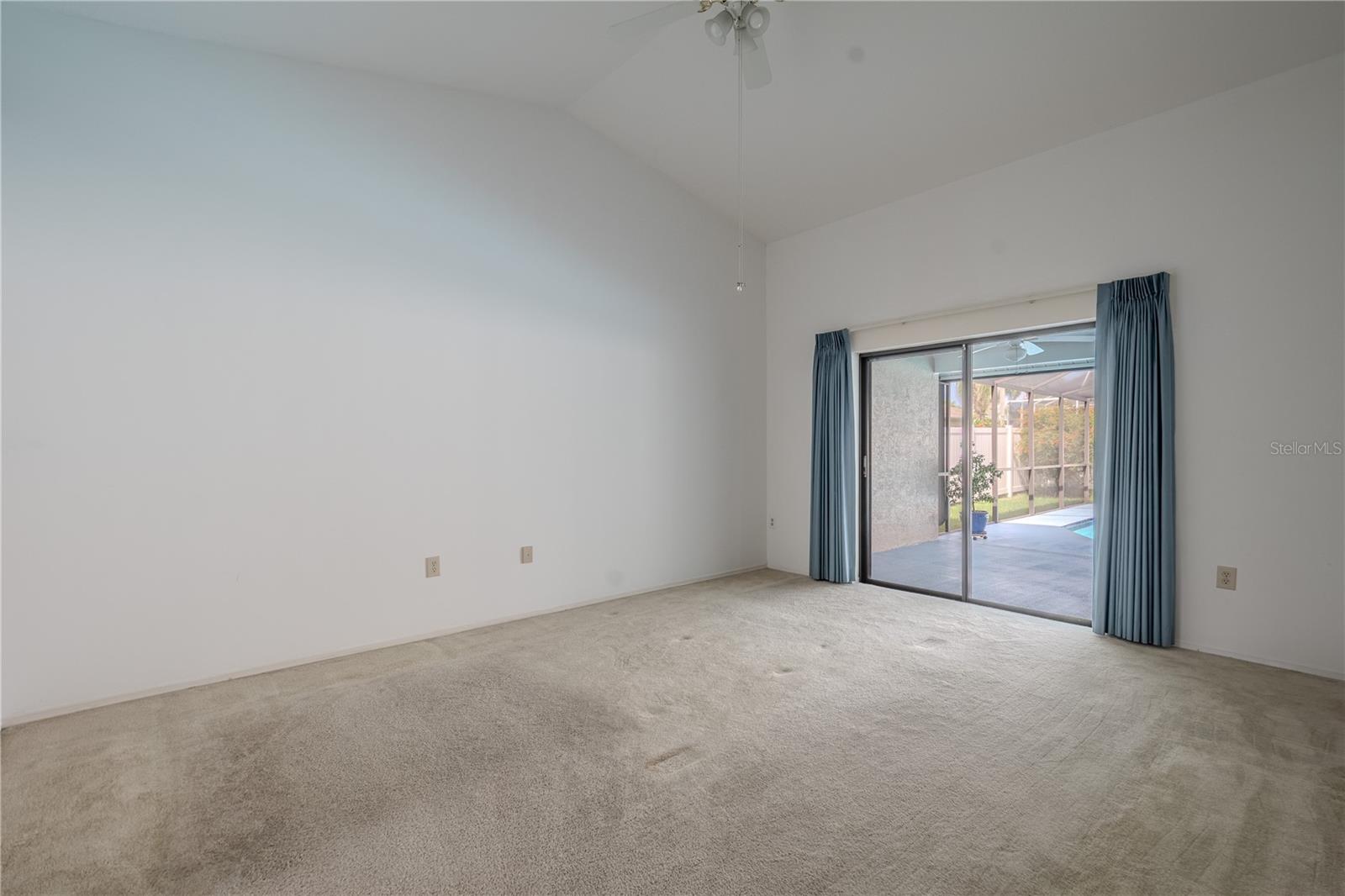 The spacious primary bedroom gives peaceful views and direct access to the screened lanai and pool area. Vaulted ceilings enhance the room’s open, airy feel, while plush carpet underfoot adds warmth and comfort. Glass sliders floods the space with natural light and makes it easy to step outside and enjoy a morning swim or evening breeze.
