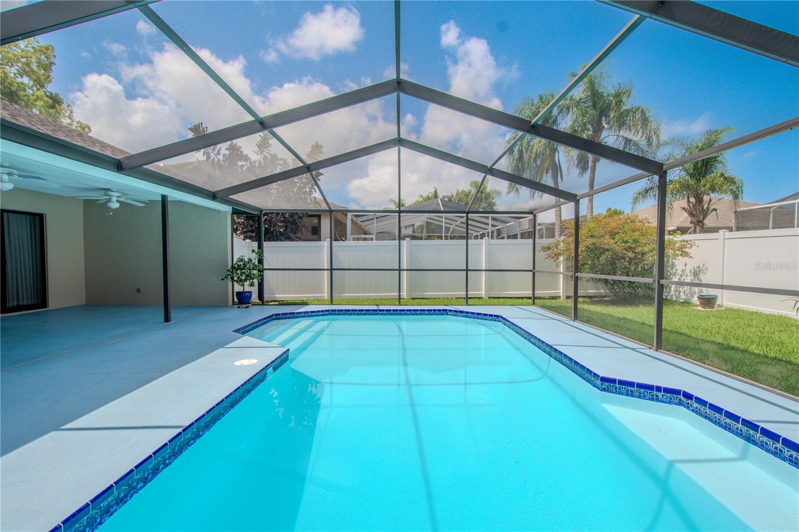 A white vinyl privacy fence installed in 2025 wraps the backyard, while the clear-screen enclosure overhead ensures bug-free enjoyment.