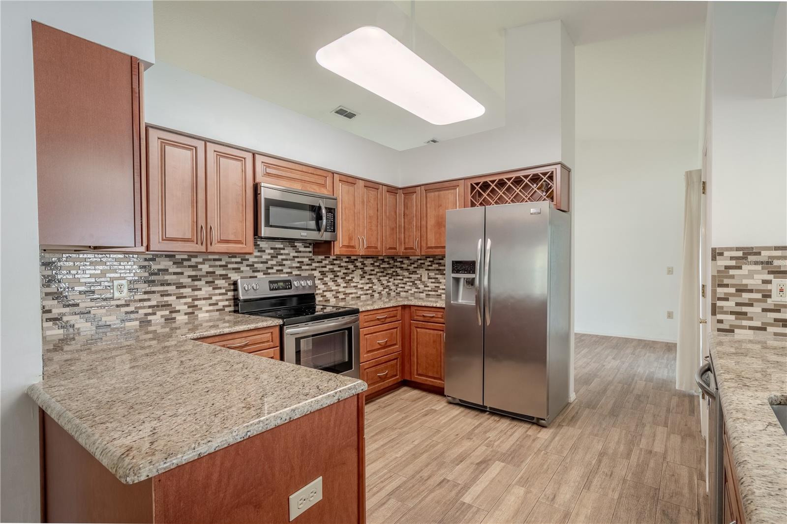 Featuring rich wood cabinetry with elegant raised-panel doors, granite countertops, and a stunning mosaic tile backsplash that adds texture and dimension, the space blends warmth with modern appeal.