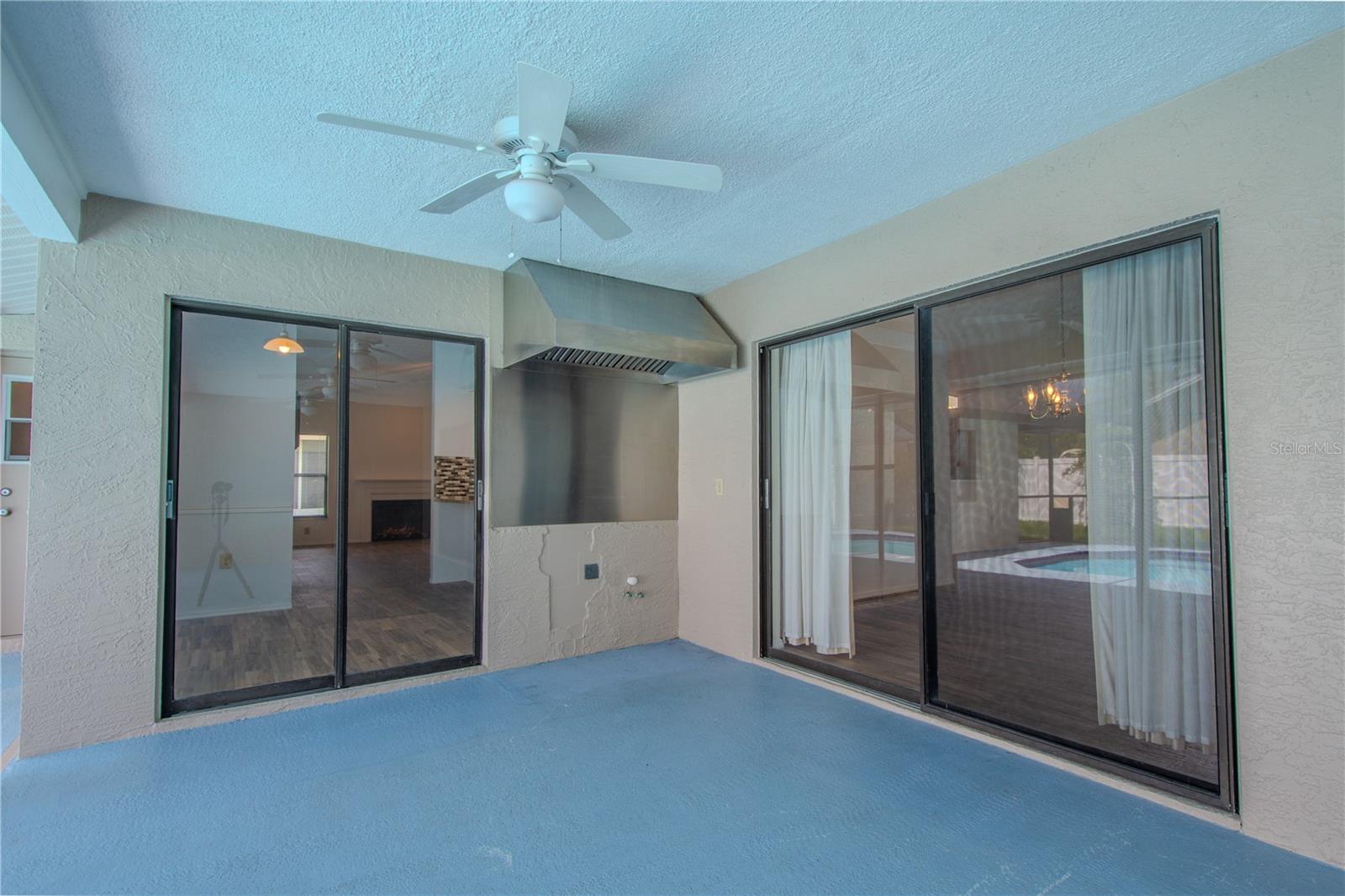 spacious covered lanai—your all-season outdoor retreat. This versatile space is equipped with a Trade-Wind stainless steel BBQ range hood, offering serious grilling potential and ventilation for an outdoor kitchen setup. Whether you're envisioning a full summer kitchen or just a cozy space to relax poolside, this area is wired and ready. With dual sliding glass doors providing seamless access from both the living and dining areas, plus a ceiling fan overhead for added comfort, this patio blends functionality and leisure—perfect for Florida-style indoor-outdoor living.