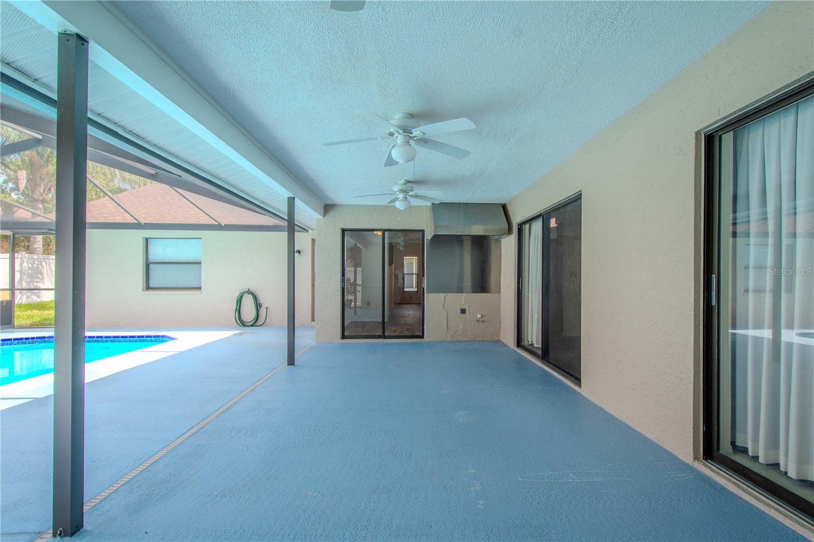 Spacious covered lanai—your all-season outdoor retreat. This versatile space is equipped with a Trade-Wind stainless steel BBQ range hood, offering serious grilling potential and ventilation for an outdoor kitchen setup. Whether you're envisioning a full summer kitchen or just a cozy space to relax poolside, this area is wired and ready. With dual sliding glass doors providing seamless access from both the living and dining areas, plus a ceiling fan overhead for added comfort, this patio blends functionality and leisure—perfect for Florida-style indoor-outdoor living.