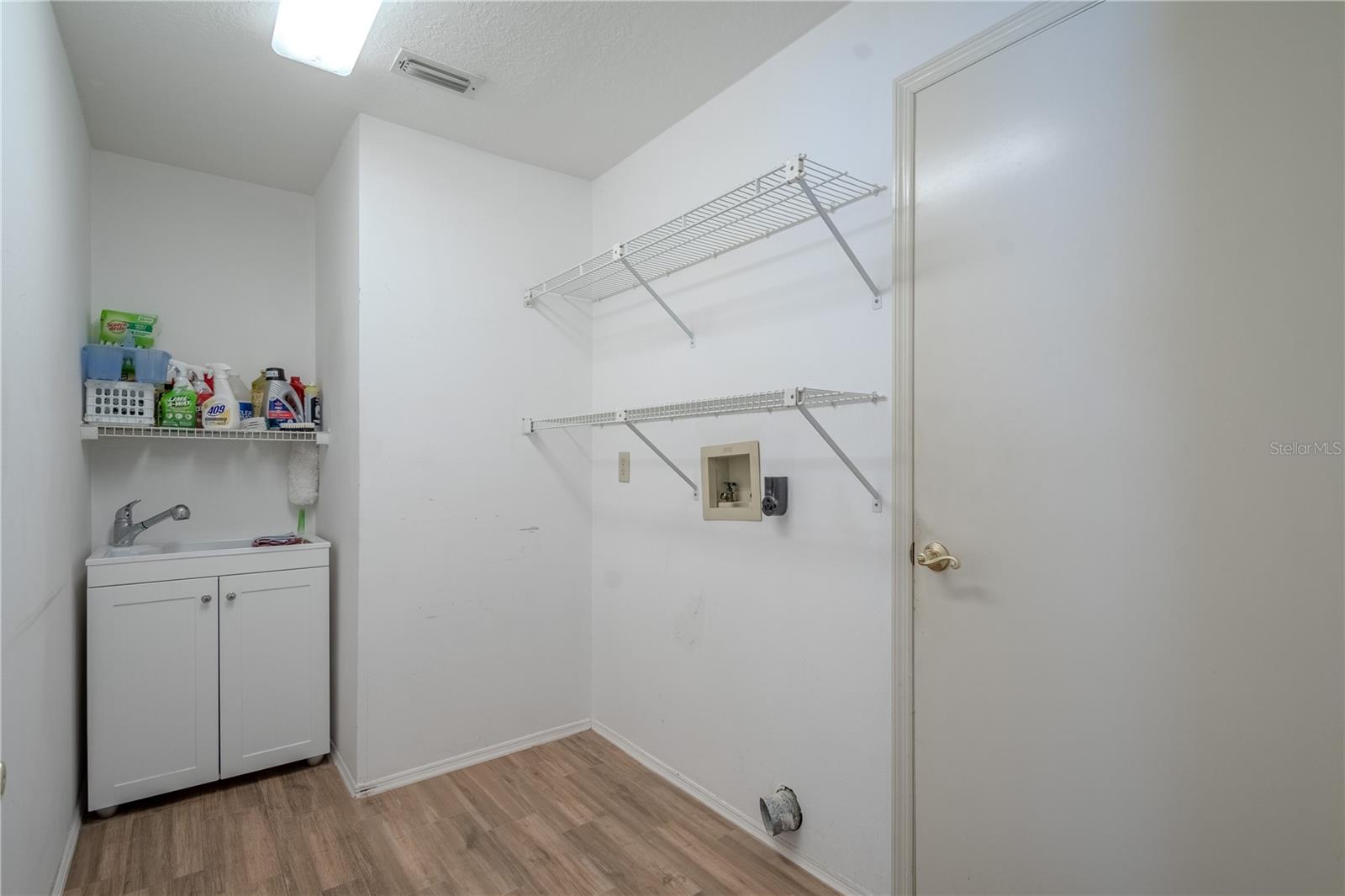 Conveniently located inside the home, the laundry room offers ample space and functionality with upper shelving for storage and organization. A utility sink adds extra practicality for hand-washing and clean-up tasks. With dedicated washer and dryer hookups and easy-to-clean wood-look flooring, this space is both efficient and accessible—ready to handle your everyday laundry needs with ease.