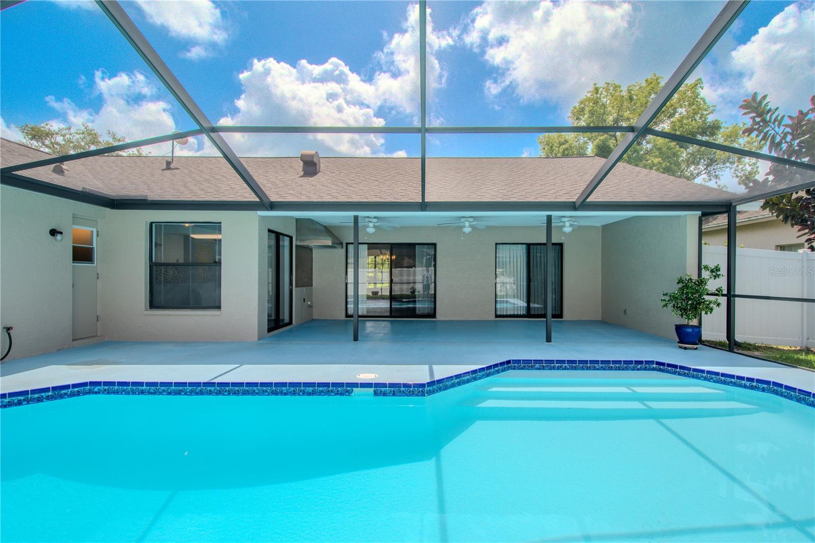 Screen-enclosed back patio and pool area, showcasing the seamless blend of indoor-outdoor living. The sparkling turquoise pool, accented with classic blue tile trim, is the focal point—inviting relaxation under the Florida sun.