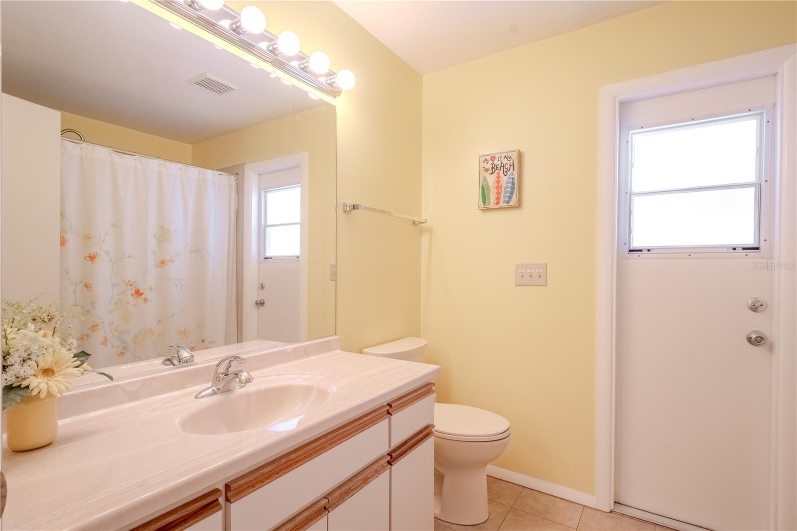 The second full bath offers bright, functional convenience with easy access to the pool and lanai—perfect for rinsing off after a swim or entertaining guests outdoors. A cheerful splash of color brings warmth to the space, while the oversized vanity with ample counter space and a wide mirror ensures plenty of room for daily routines.