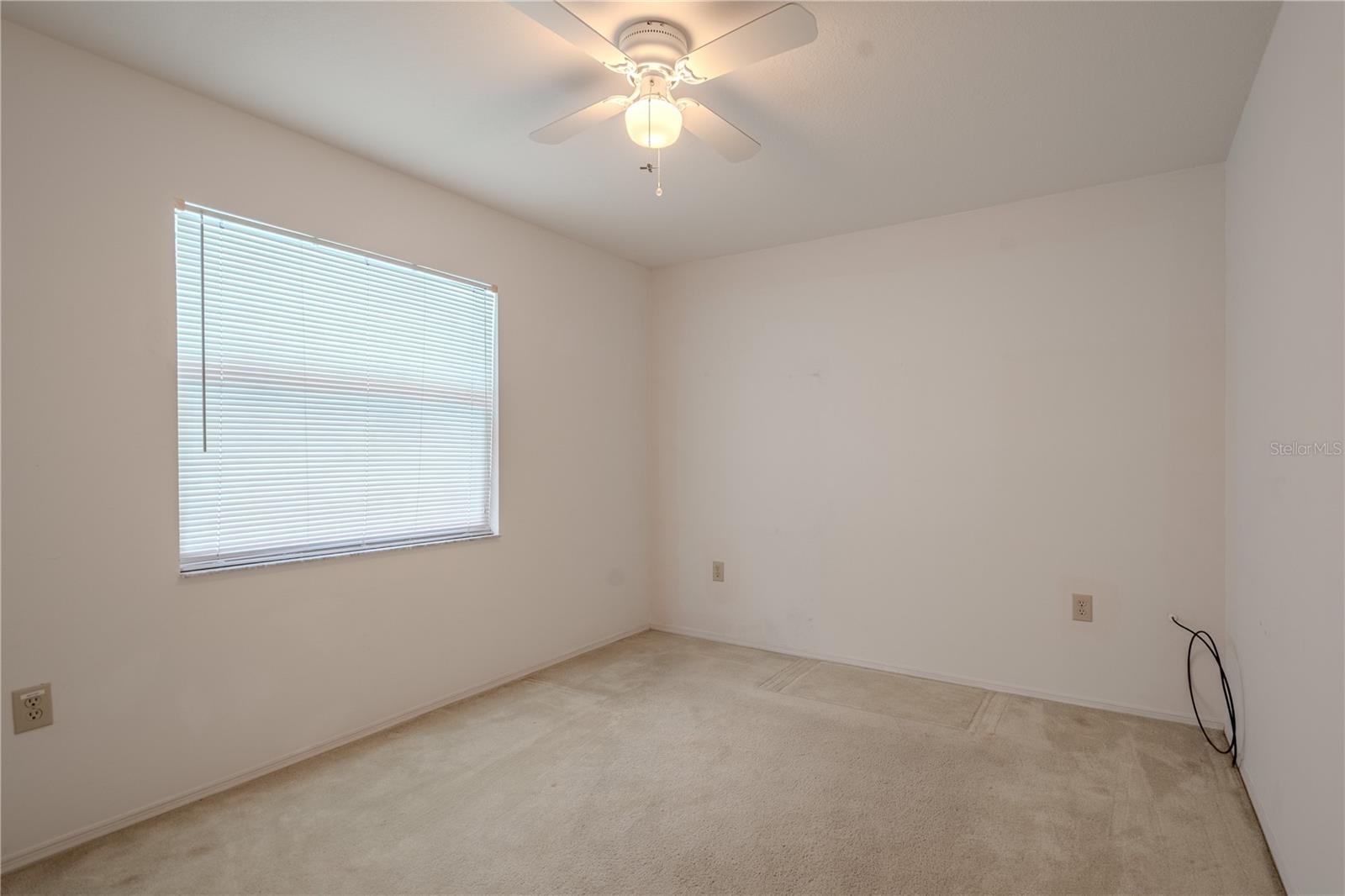 Bedroom 2 offers a quiet, comfortable space ideal for guests, a home office, or a cozy retreat. A large window fills the room with soft natural light, while a ceiling fan overhead ensures year-round comfort.