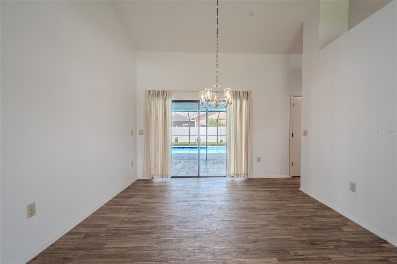 Anchored by a classic chandelier and framed by floor-to-ceiling sliding glass doors, the space is bathed in natural light and offers beautiful views of the screened-in pool and patio—creating the perfect backdrop for entertaining or enjoying a peaceful meal at home