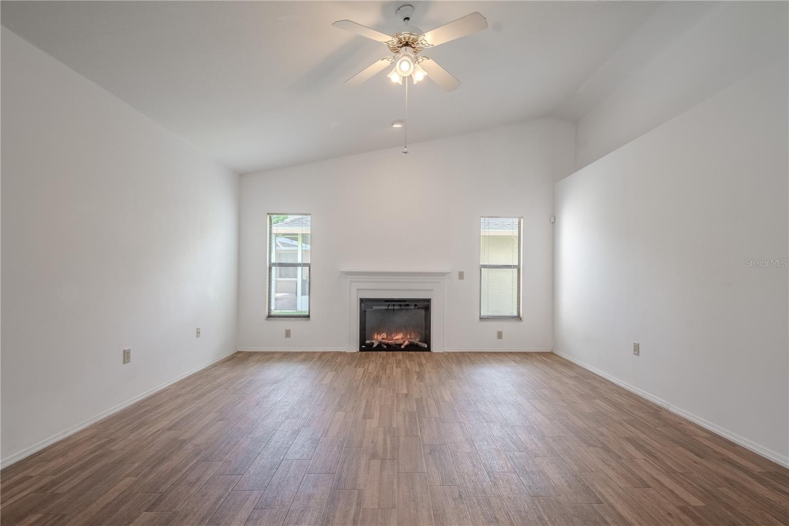 A charming fireplace—once wood-burning, now thoughtfully converted to electric in 2025—offering cozy ambiance at the flip of a switch, with no mess or hassle.Wood-look tile flooring continues here for a cohesive and low-maintenance living space, and a ceiling fan adds year-round comfort.