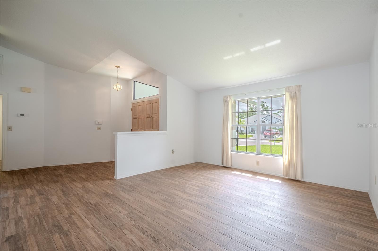 The continuous wood-look tile floors create a seamless, low-maintenance foundation, while the vaulted ceiling enhances the sense of openness and space. With its clean lines, neutral palette, and airy ambiance, this versatile room is a blank canvas—perfect for a cozy sitting area, formal entertaining, or a tranquil reading nook.