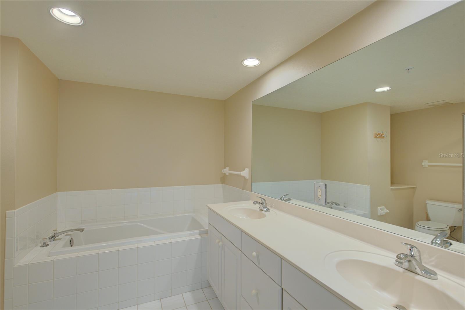 dual sinks and a large soaking tub with clean white tile throughout.
