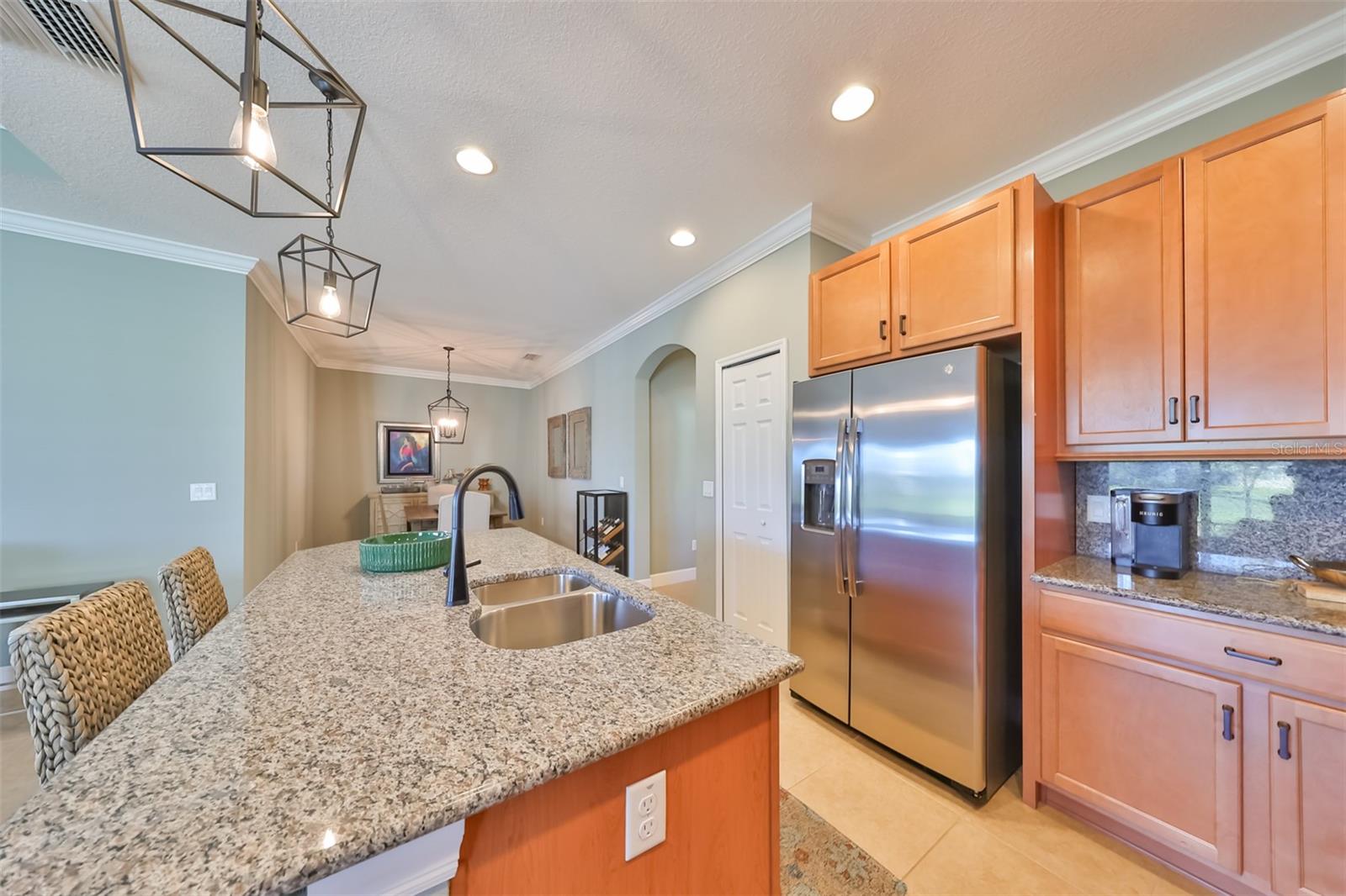 A large center island with a granite countertop and a spacious breakfast bar provides enormous counter space.  Notice the matching granite backsplash.