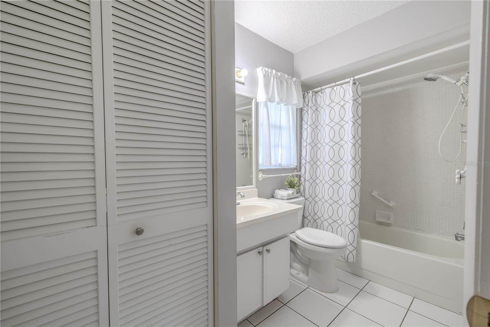 The shower includes a handheld fixture and grab bars for added convenience. The large vanity mirror and overhead lighting provide a spacious feel, and a linen closet is located just outside the bathroom for extra storage. Perfectly practical with a fresh, timeless look.