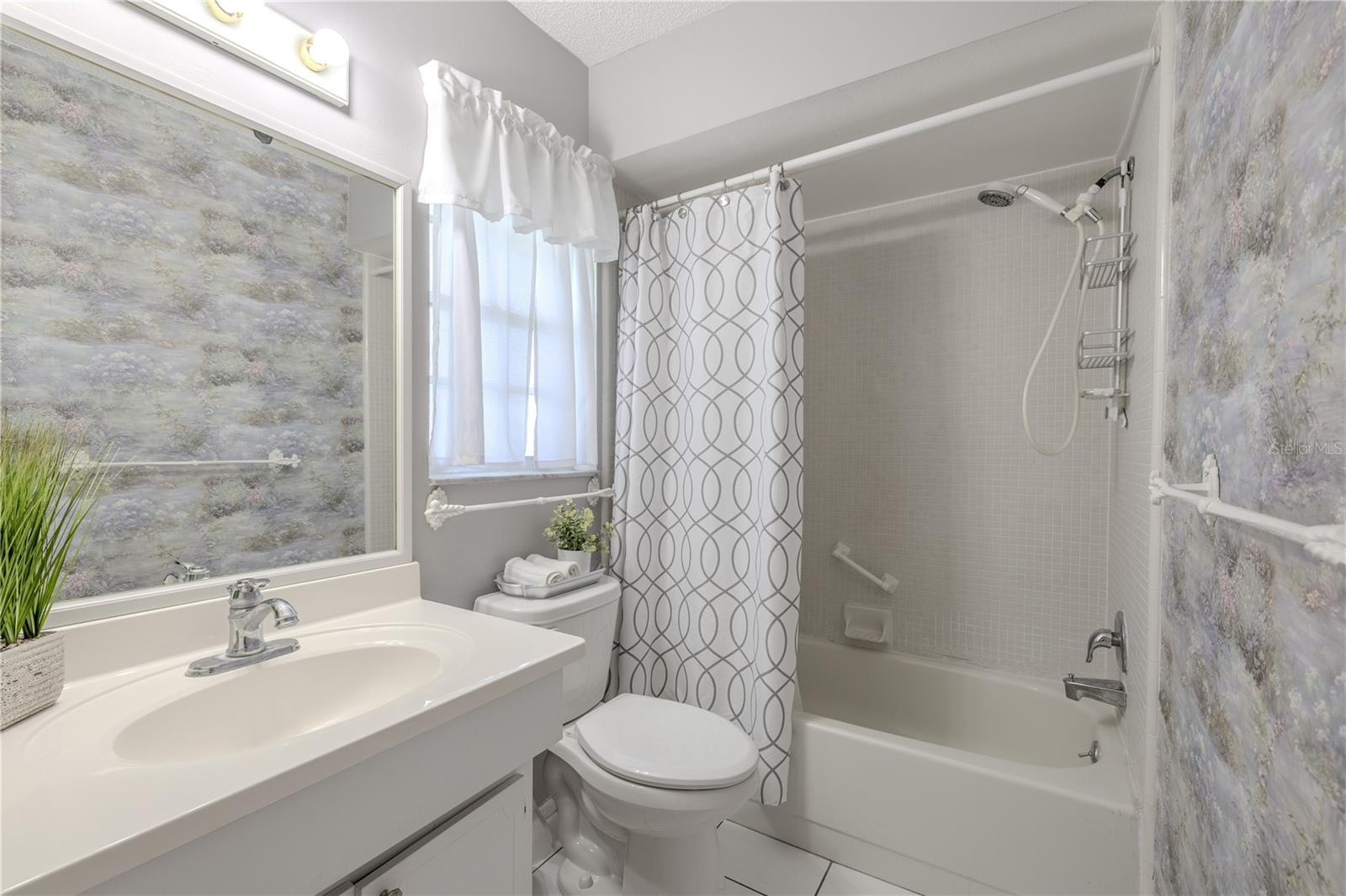 This bright and well-maintained bathroom features a clean, neutral design with a combination tub and shower, tile flooring, and a large vanity with integrated sink.