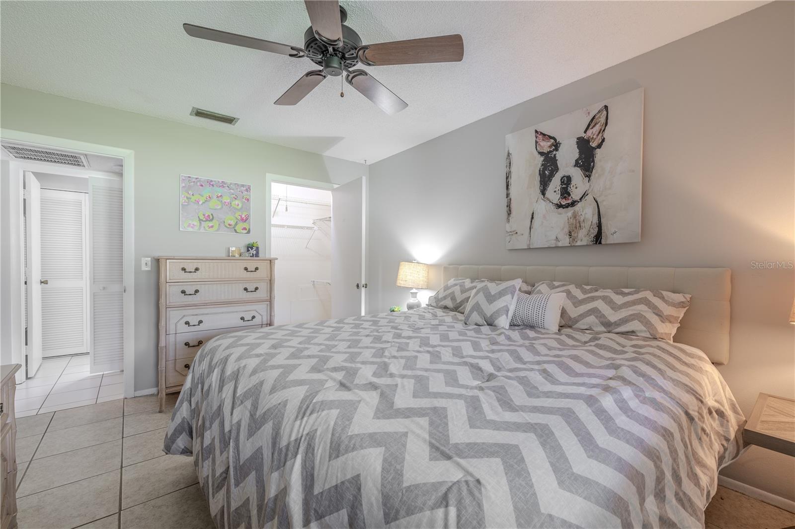 The spacious bedroom features neutral tile flooring, soft wall tones, and a ceiling fan for year-round comfort. A walk-in closet offers generous storage space. Clean lines and a calming color palette make this bedroom a serene and versatile space.