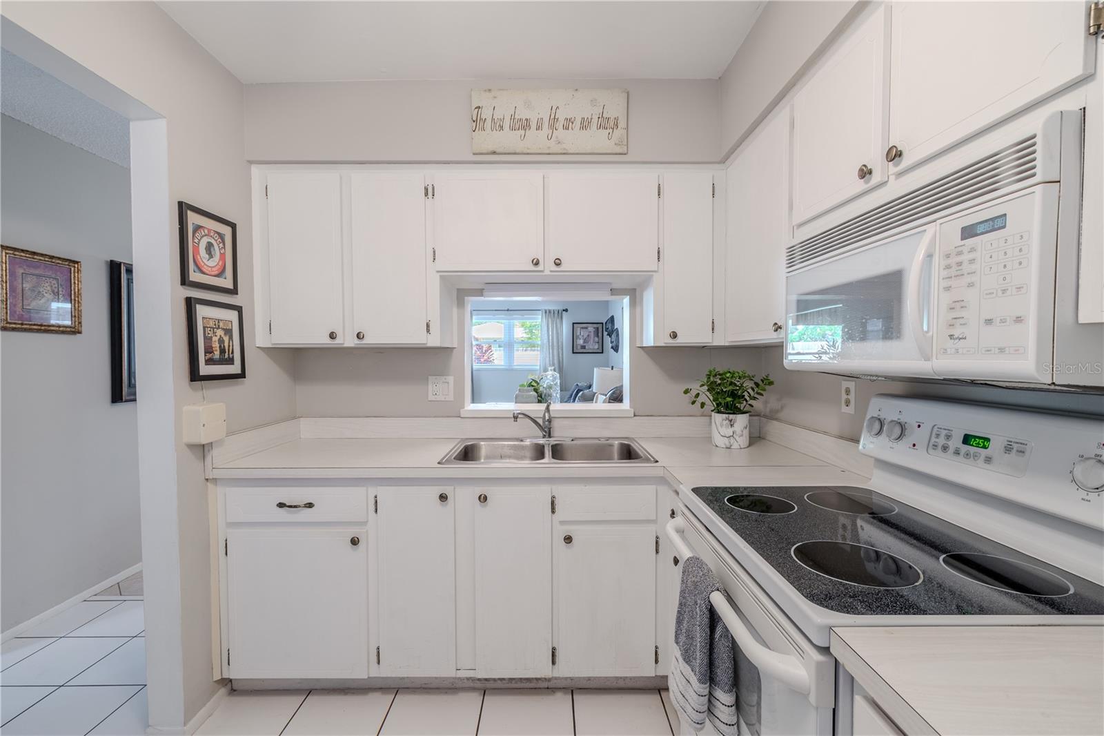 A convenient pass-through window in the kitchen opens to the living area, creating an open feel and allowing for easy entertaining. Classic cabinet hardware and fresh neutral paint provide a cohesive, move-in-ready look. Whether you're whipping up a quick meal or hosting guests, this kitchen combines functionality with a welcoming vibe.