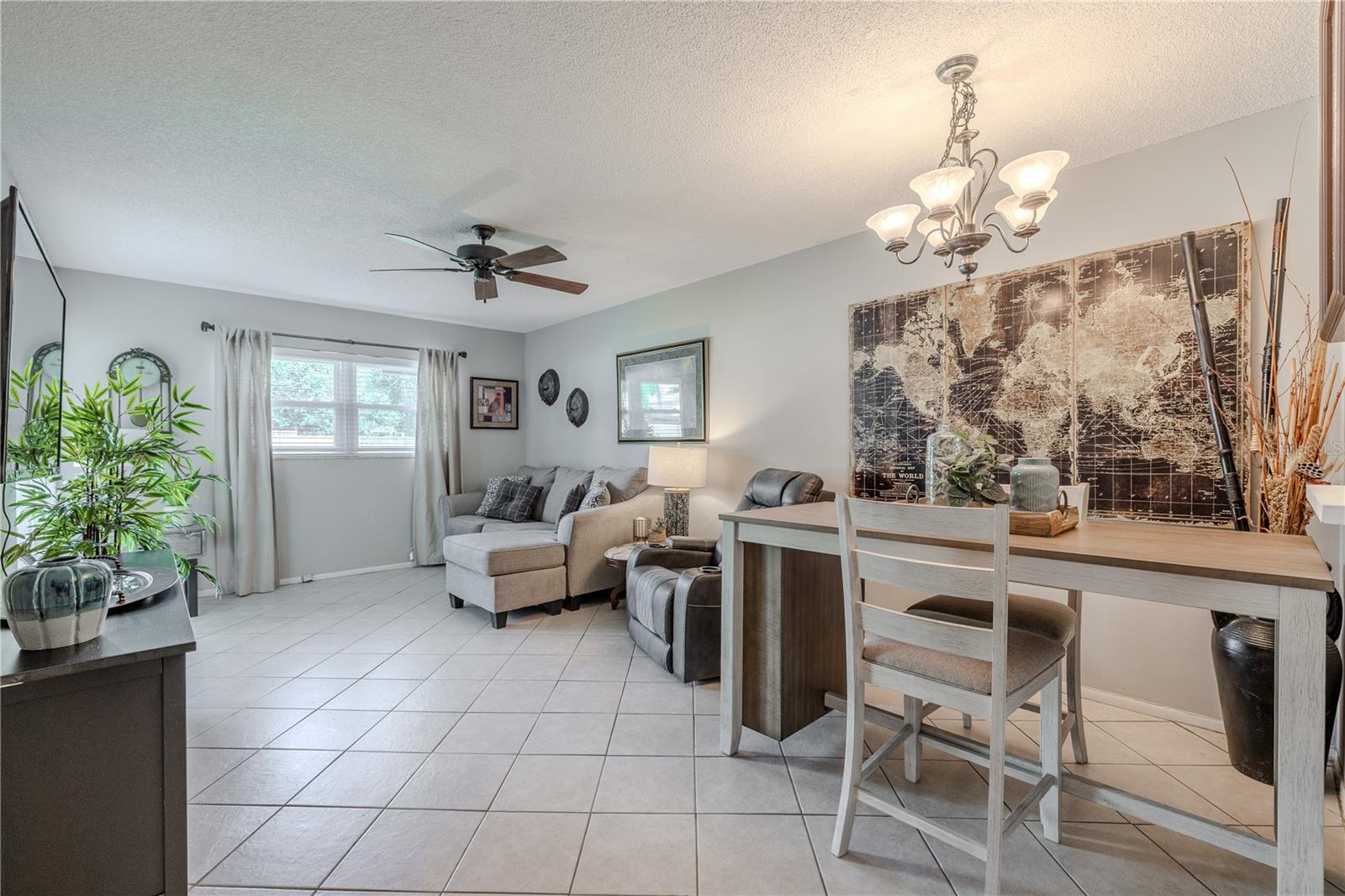This open-concept living and dining area is filled with natural light and designed for both comfort and functionality. Neutral tile flooring runs throughout, complemented by soft gray walls and a cohesive color palette that makes decorating effortless. The dining area features a modern light fixture.