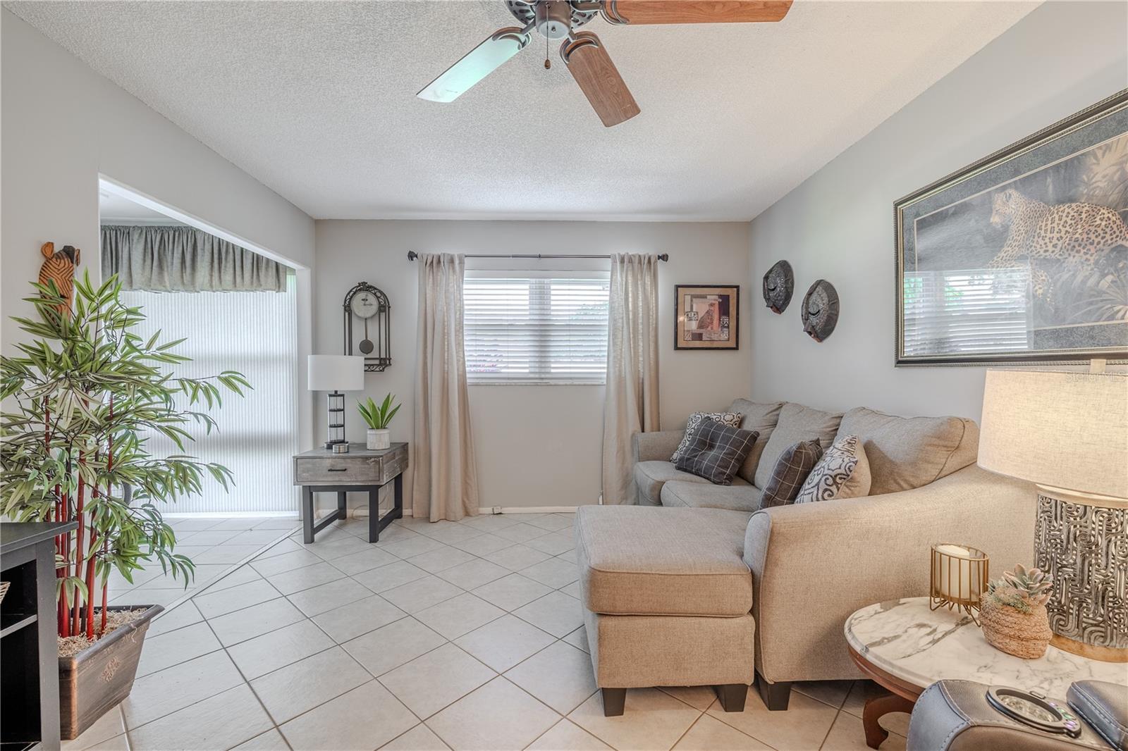 In the living room, a large window and ceiling fan enhance airflow and brightness, creating a warm and inviting atmosphere for relaxing or hosting guests.
