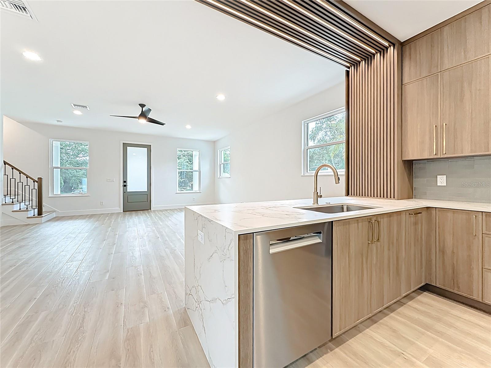 Sleek and modern kitchen featuring custom wood cabinetry, quartz waterfall countertops, stainless steel appliances, and stylish accent details — all bathed in natural light.