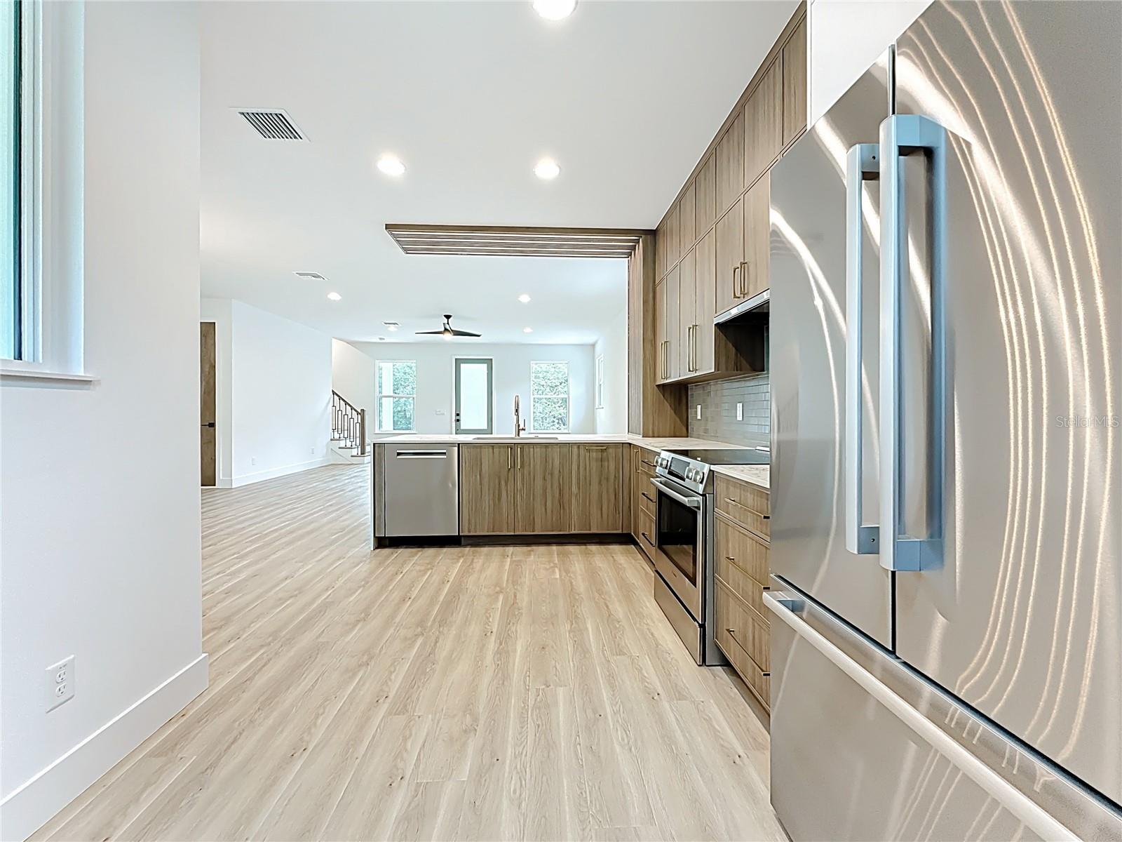 Sleek and modern kitchen featuring custom wood cabinetry, quartz waterfall countertops, stainless steel appliances, and stylish accent details — all bathed in natural light.