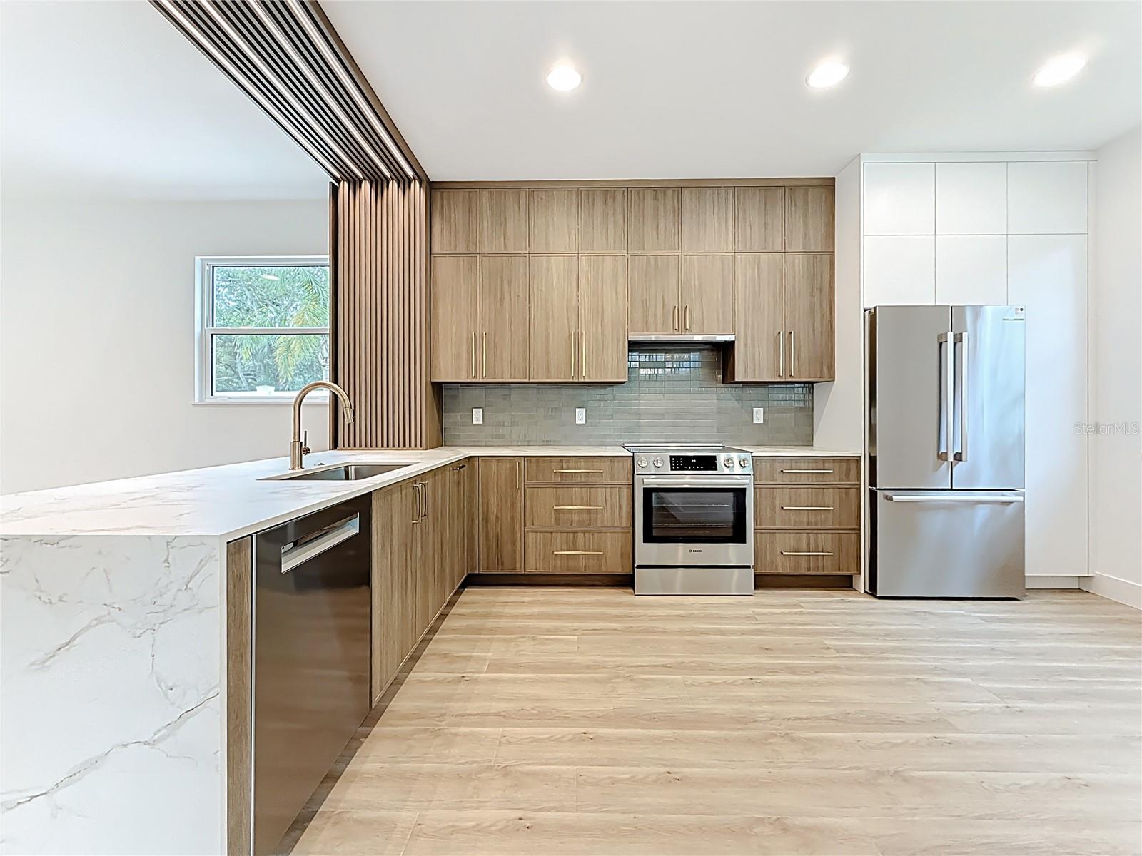 Sleek and modern kitchen featuring custom wood cabinetry, quartz waterfall countertops, stainless steel appliances, and stylish accent details — all bathed in natural light.