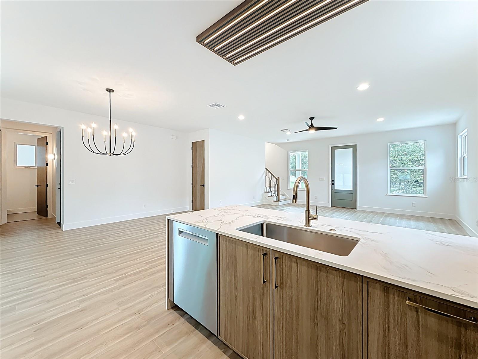 Sleek and modern kitchen featuring custom wood cabinetry, quartz waterfall countertops, stainless steel appliances, and stylish accent details — all bathed in natural light.