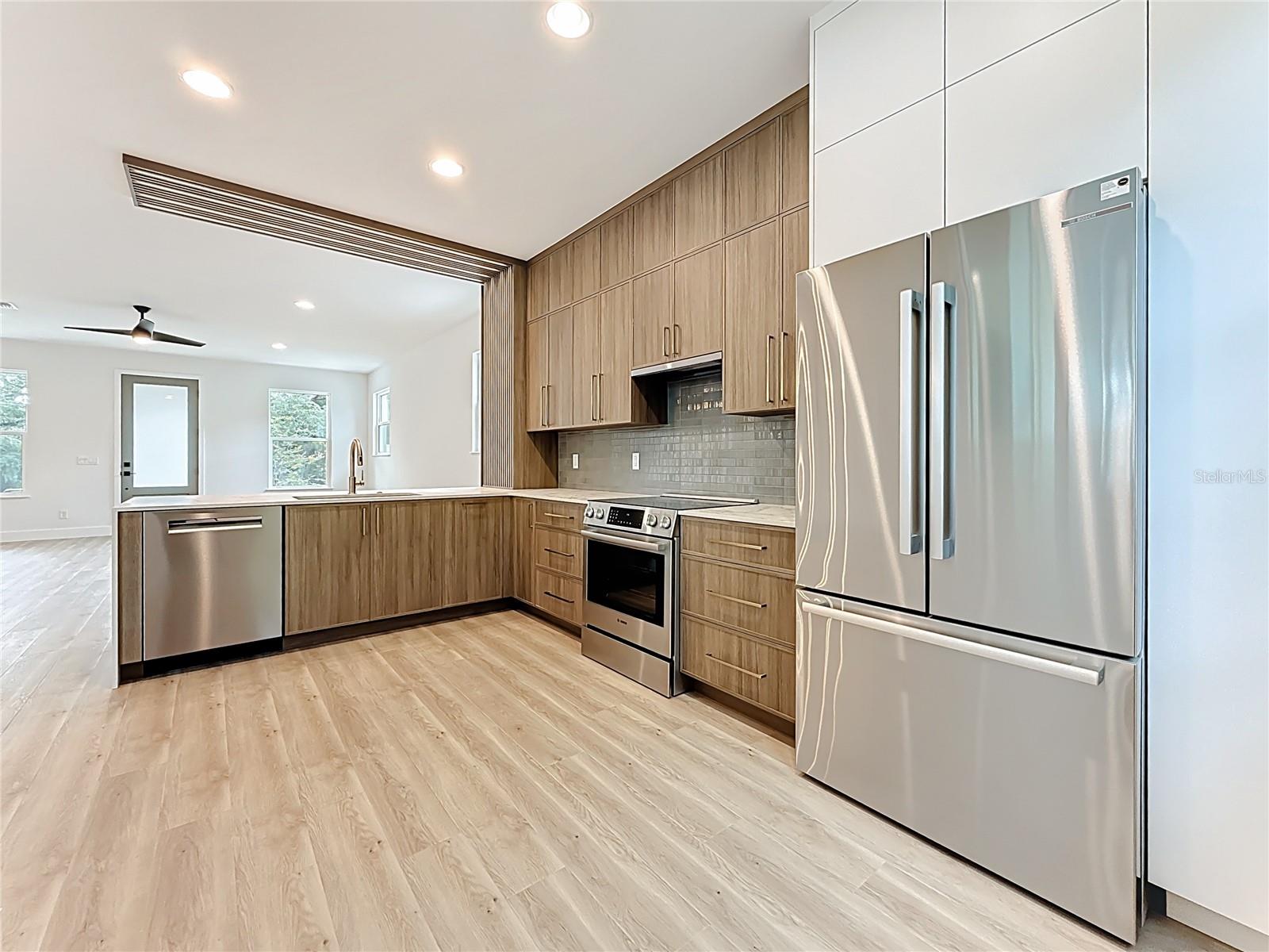 Sleek and modern kitchen featuring custom wood cabinetry, quartz waterfall countertops, stainless steel appliances, and stylish accent details — all bathed in natural light.
