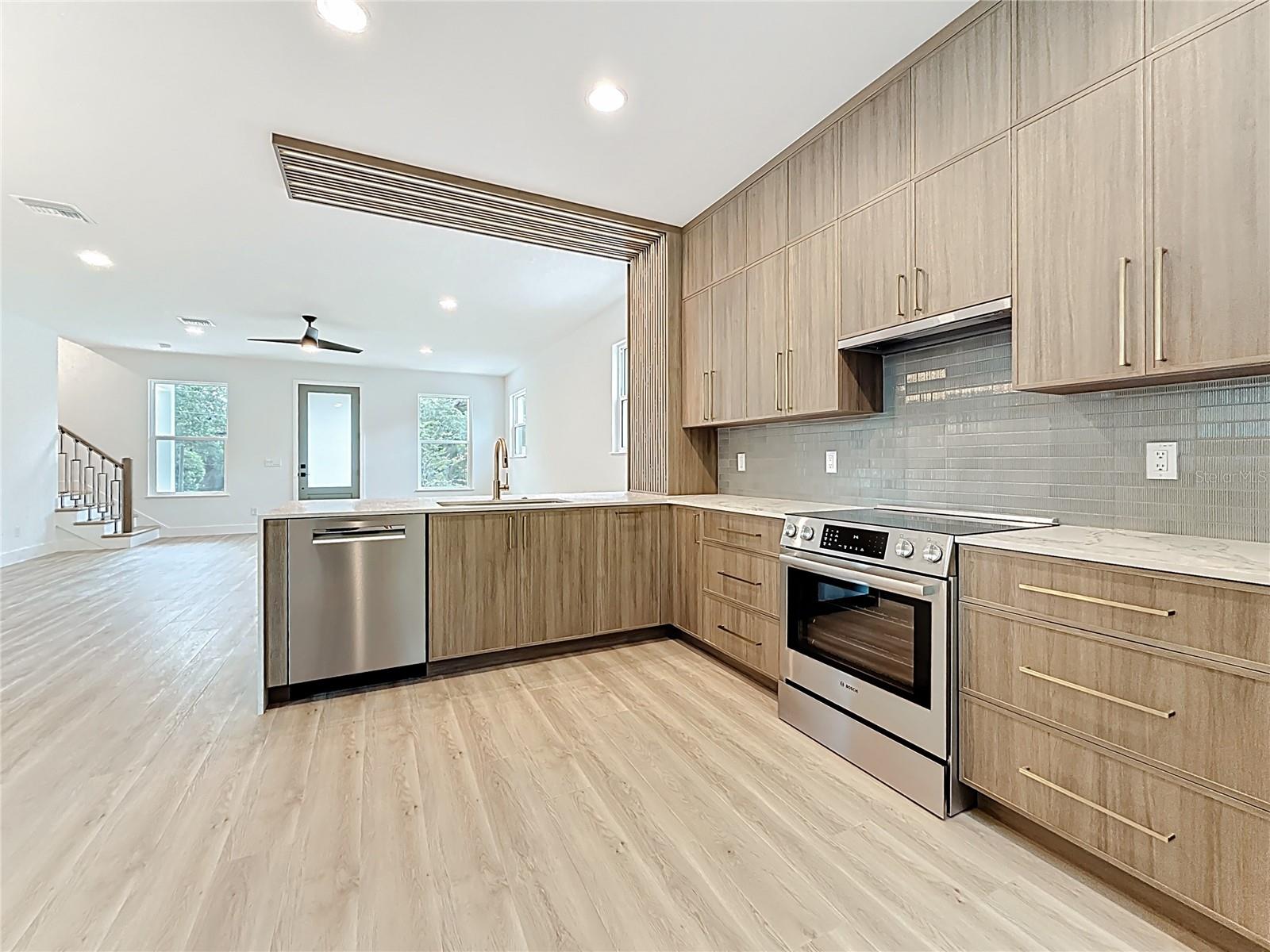 Sleek and modern kitchen featuring custom wood cabinetry, quartz waterfall countertops, stainless steel appliances, and stylish accent details — all bathed in natural light.