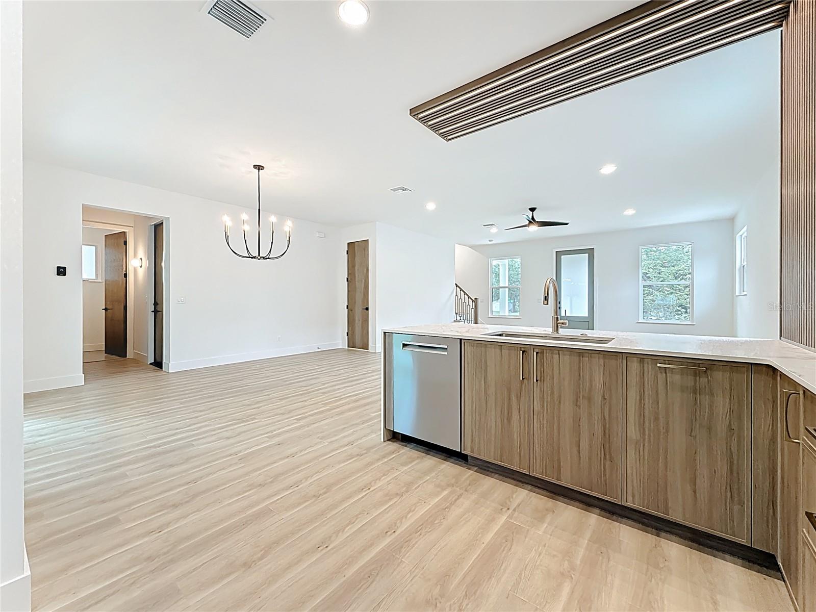 Sleek and modern kitchen featuring custom wood cabinetry, quartz waterfall countertops, stainless steel appliances, and stylish accent details — all bathed in natural light.