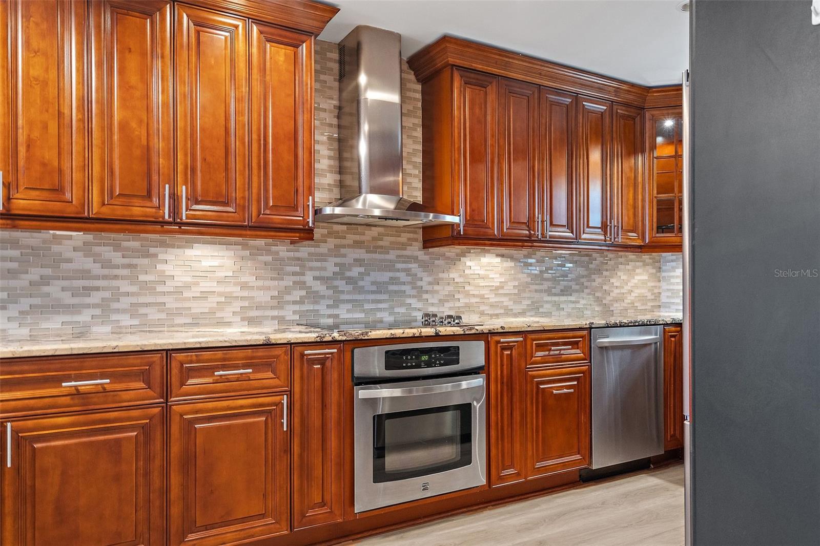 Stainless steel appliances, wood cabinetry and granite countertops with tile backsplash
