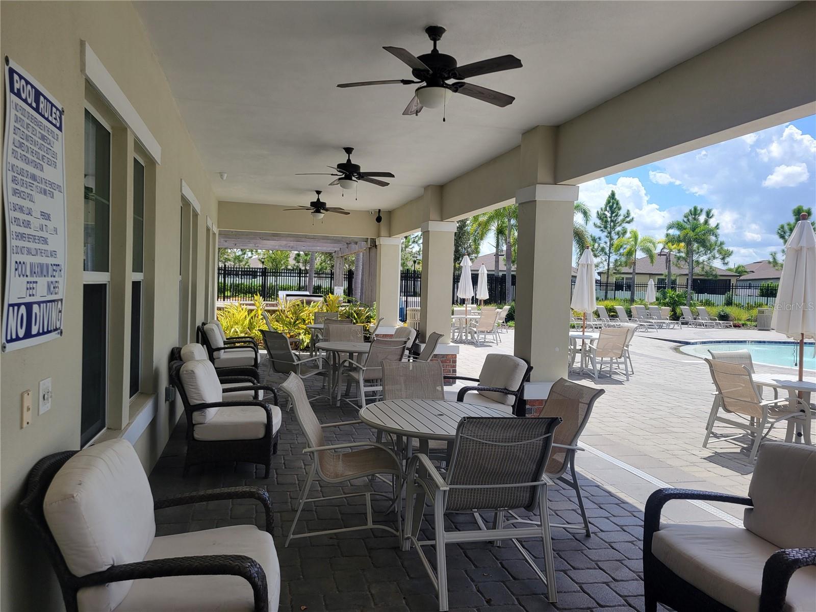 Umbrella tables, pool-side lounge chairs, and a covered patio with ceiling fans